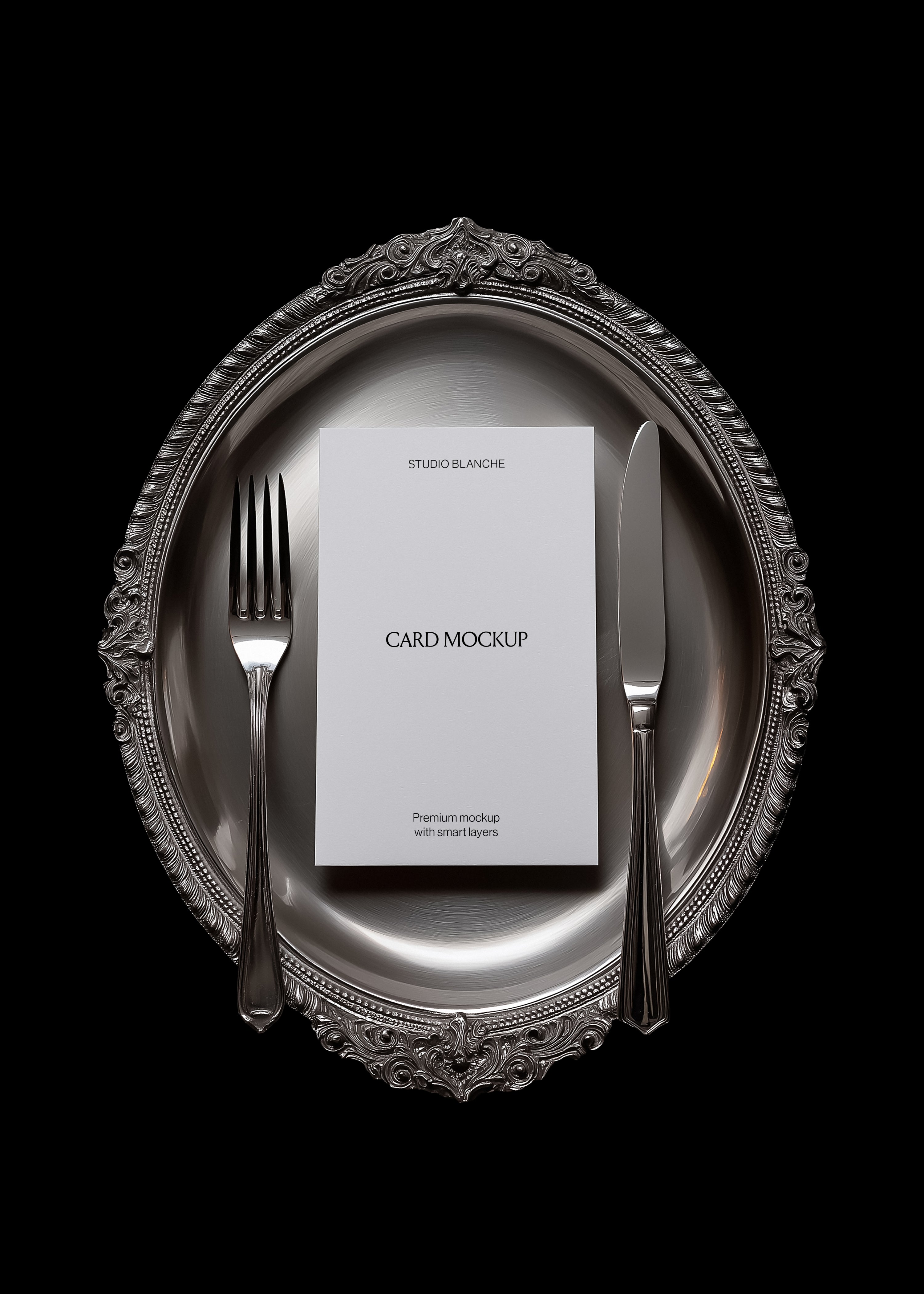Card mockup detail on baroque silver charger showing engraved rim, polished cutlery, and white card with dark text