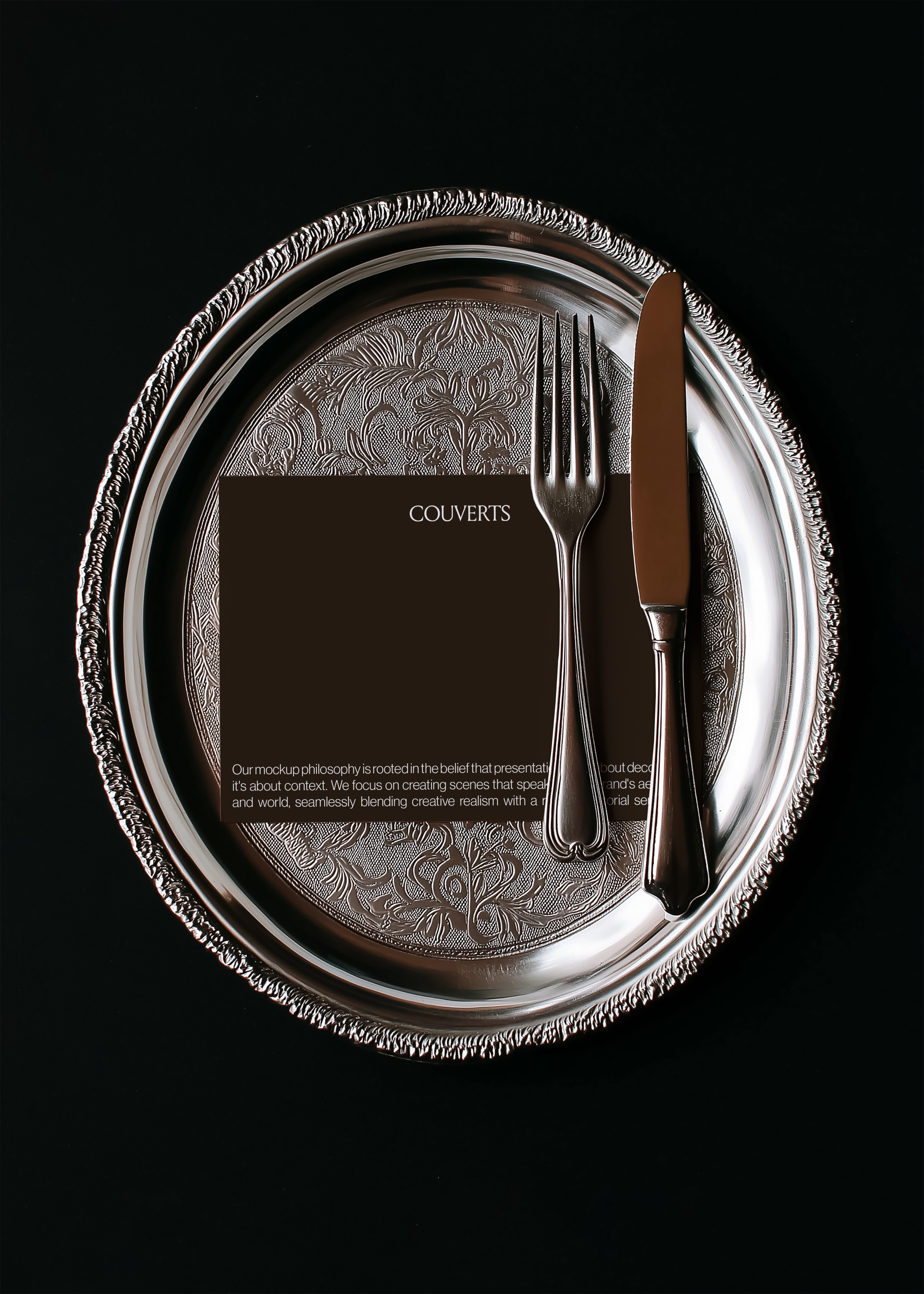 Landscape card mockup on embossed floral silver charger with dark handled fork and knife, black background, moody vintage styling