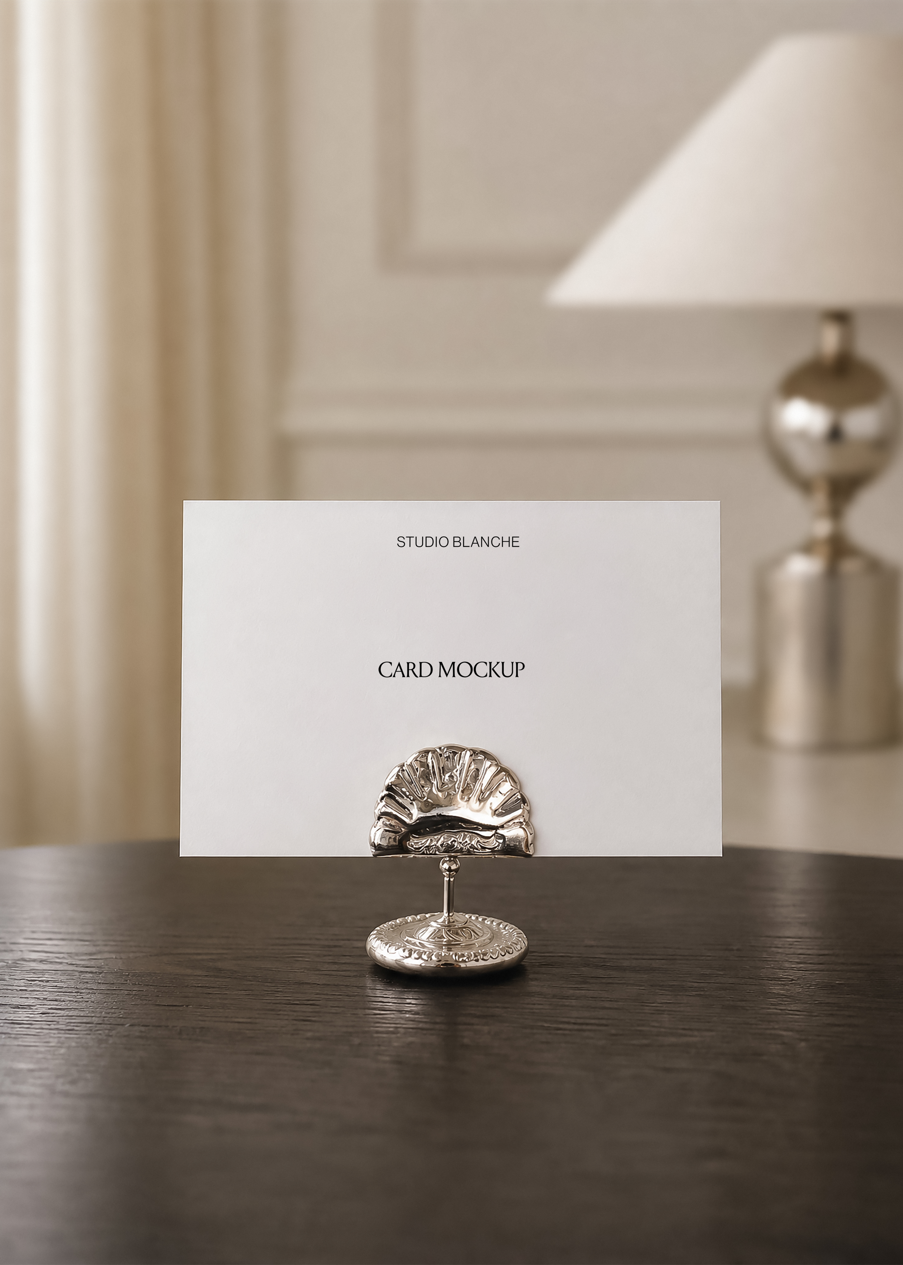 Card mockup with printed wordmark held upright in an ornate silver place card holder, panelled wall and lamp in background