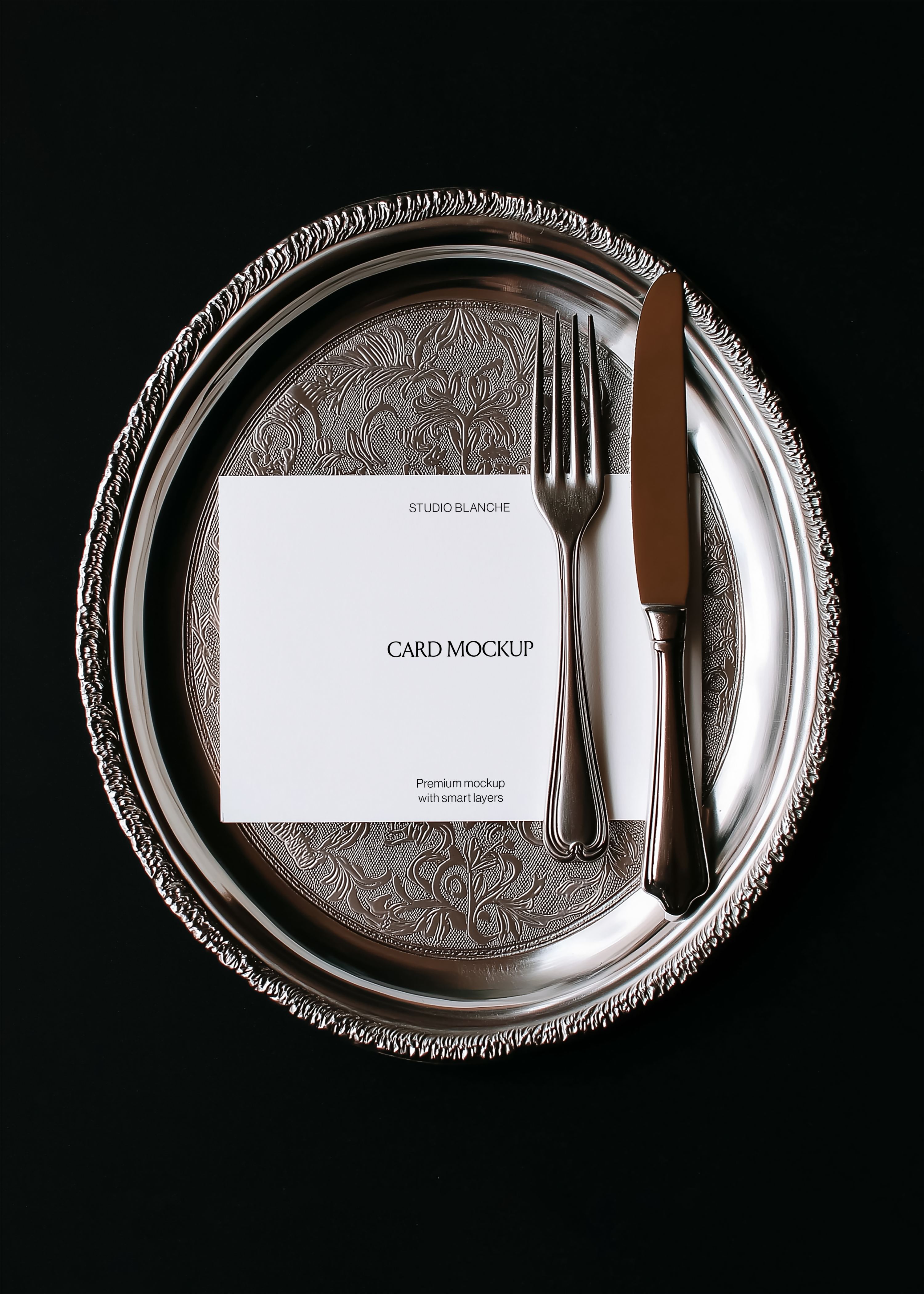 Card mockup detail showing repoussé silver charger pattern, dark handled cutlery, and white card with black text