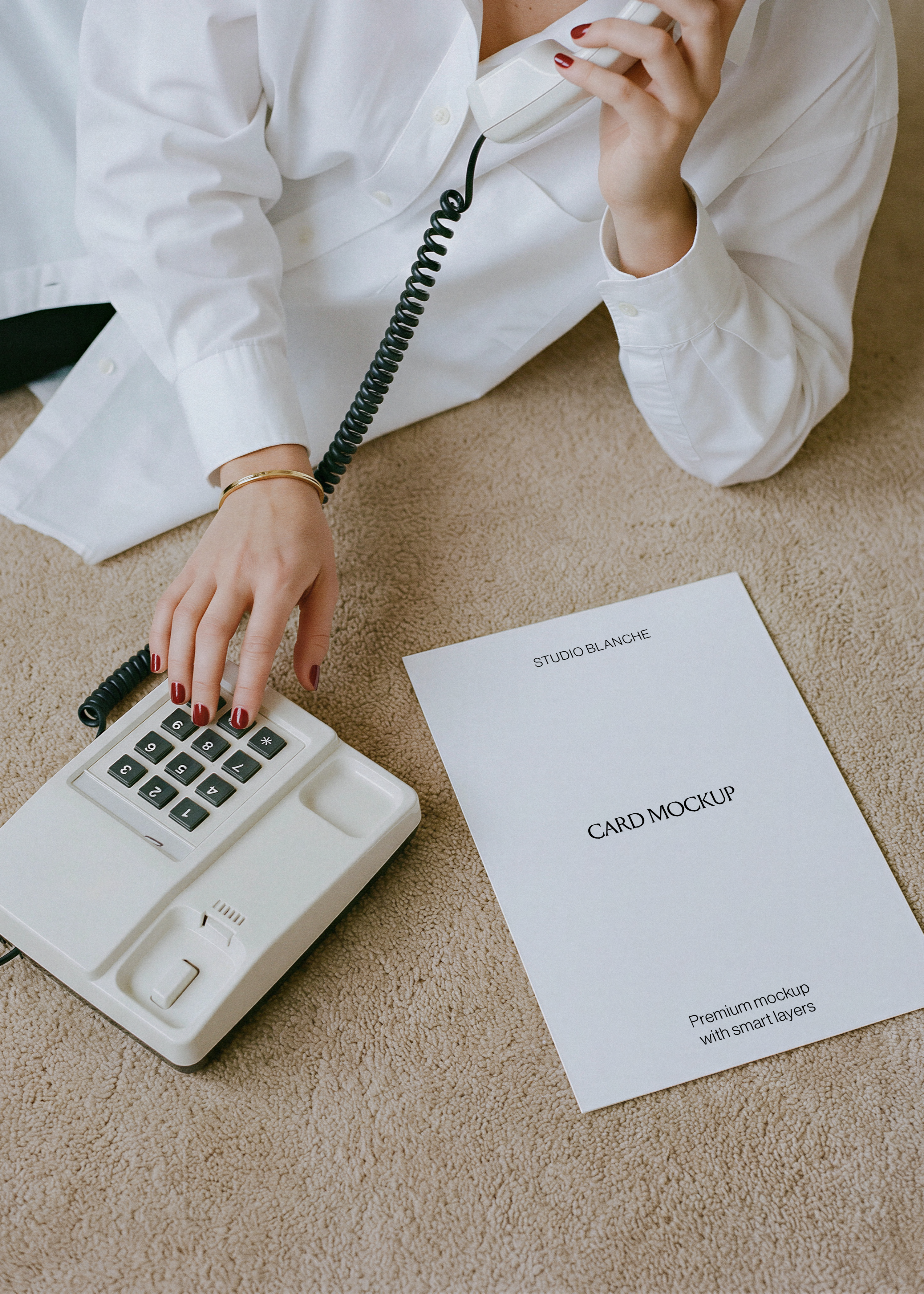 Blank A4 letterhead laid on carpet next to cream vintage telephone, white shirt sleeve and coiled cord, editorial scene