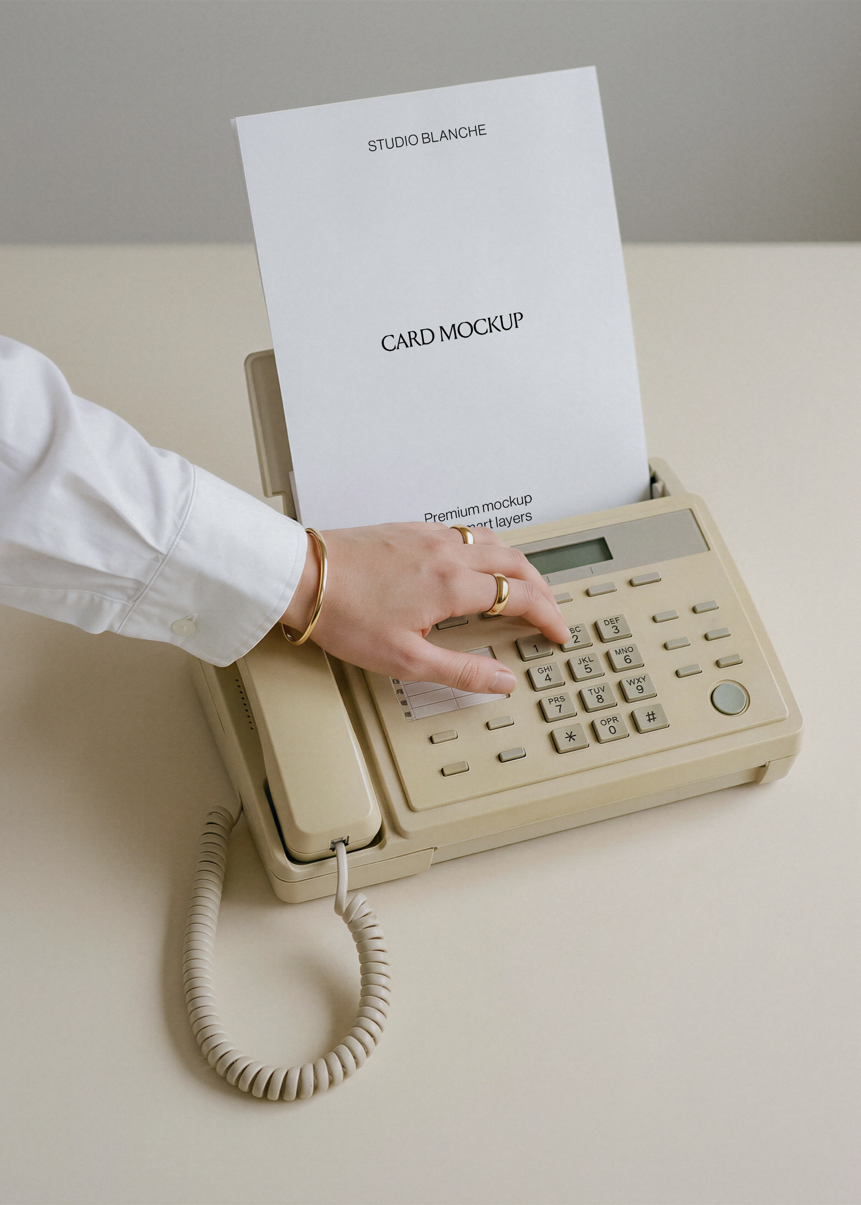 Blank A4 letterhead emerging from retro beige fax phone, coiled cord on pale desk, white shirt sleeve and gold jewellery