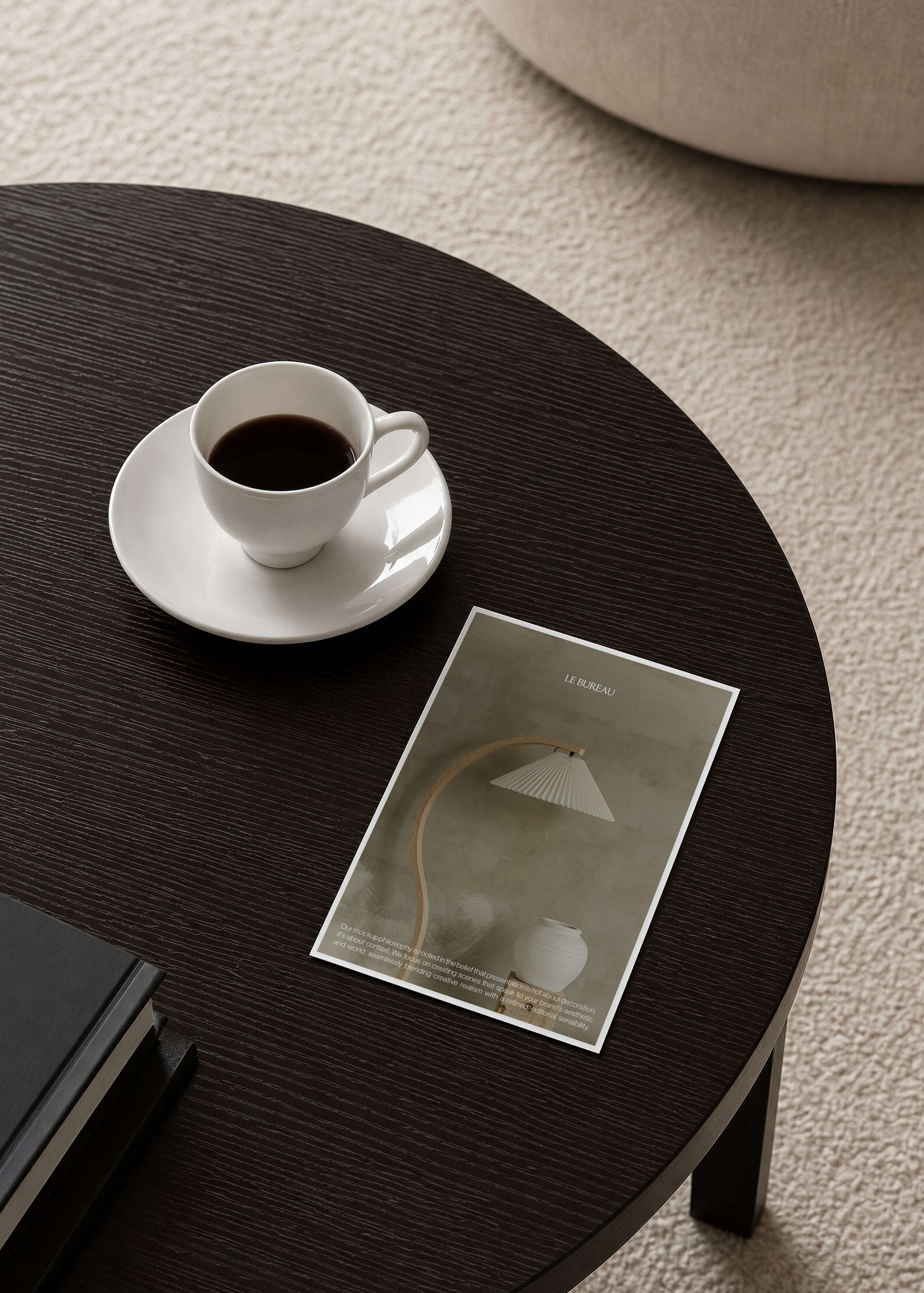 Card mockup lying flat on round dark oak table beside white espresso cup and saucer, black book and boucle rug