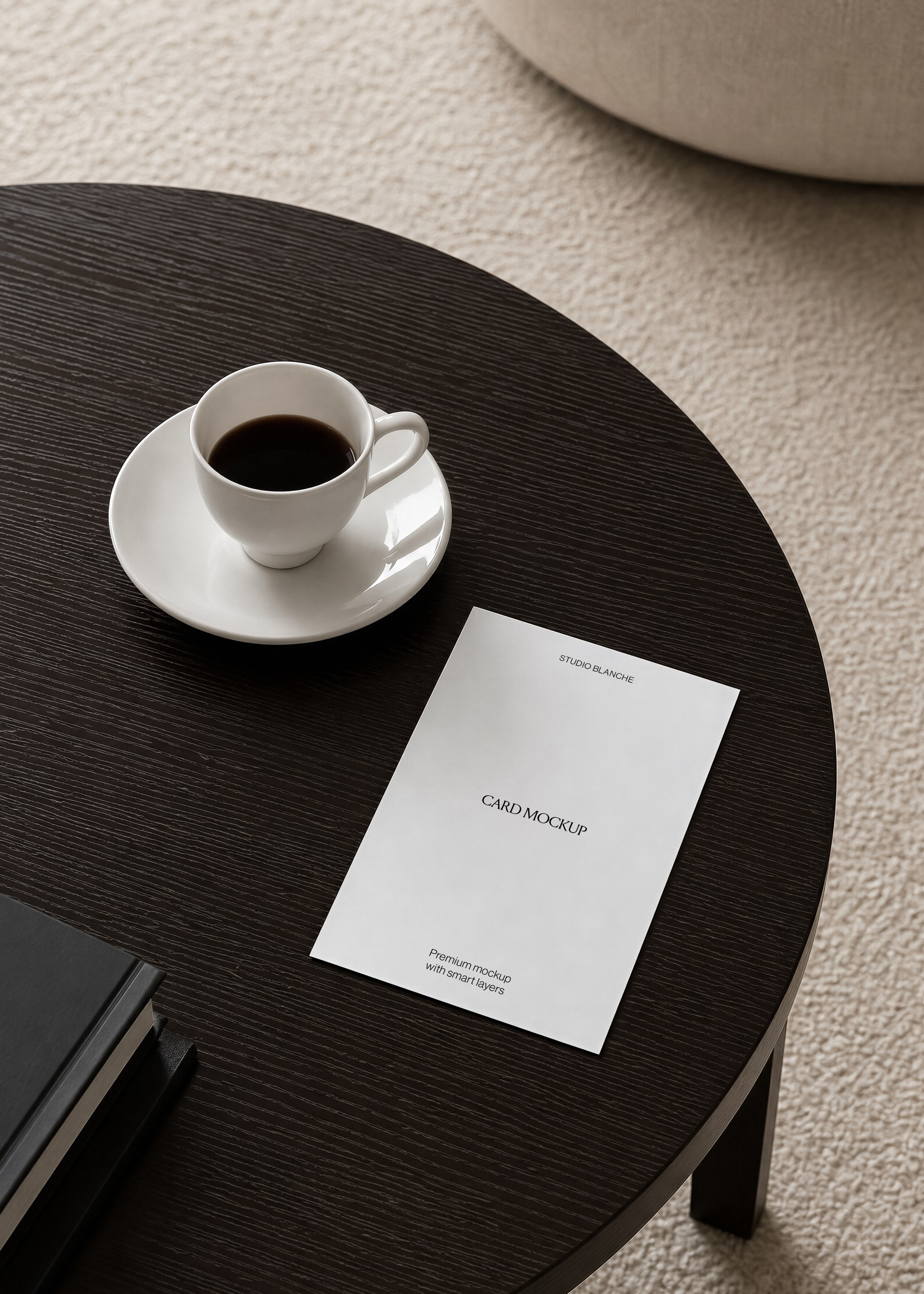 White portrait card mockup on textured dark wood tabletop, overhead view with cream pouf and looped rug below