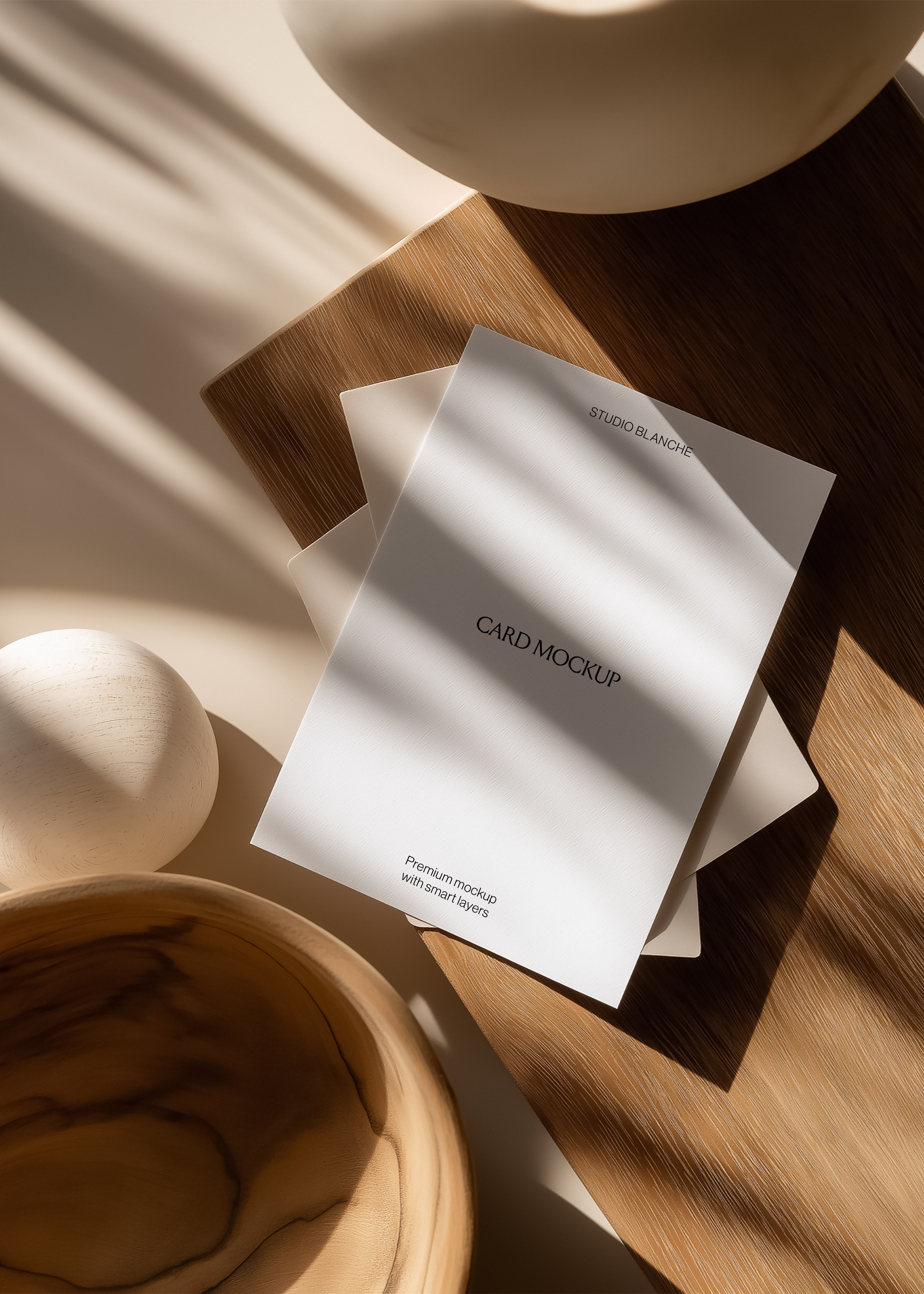 Two portrait card mockups fanned on pale oak board, matte white vase, wooden bowl and egg form, diagonal window light shadows