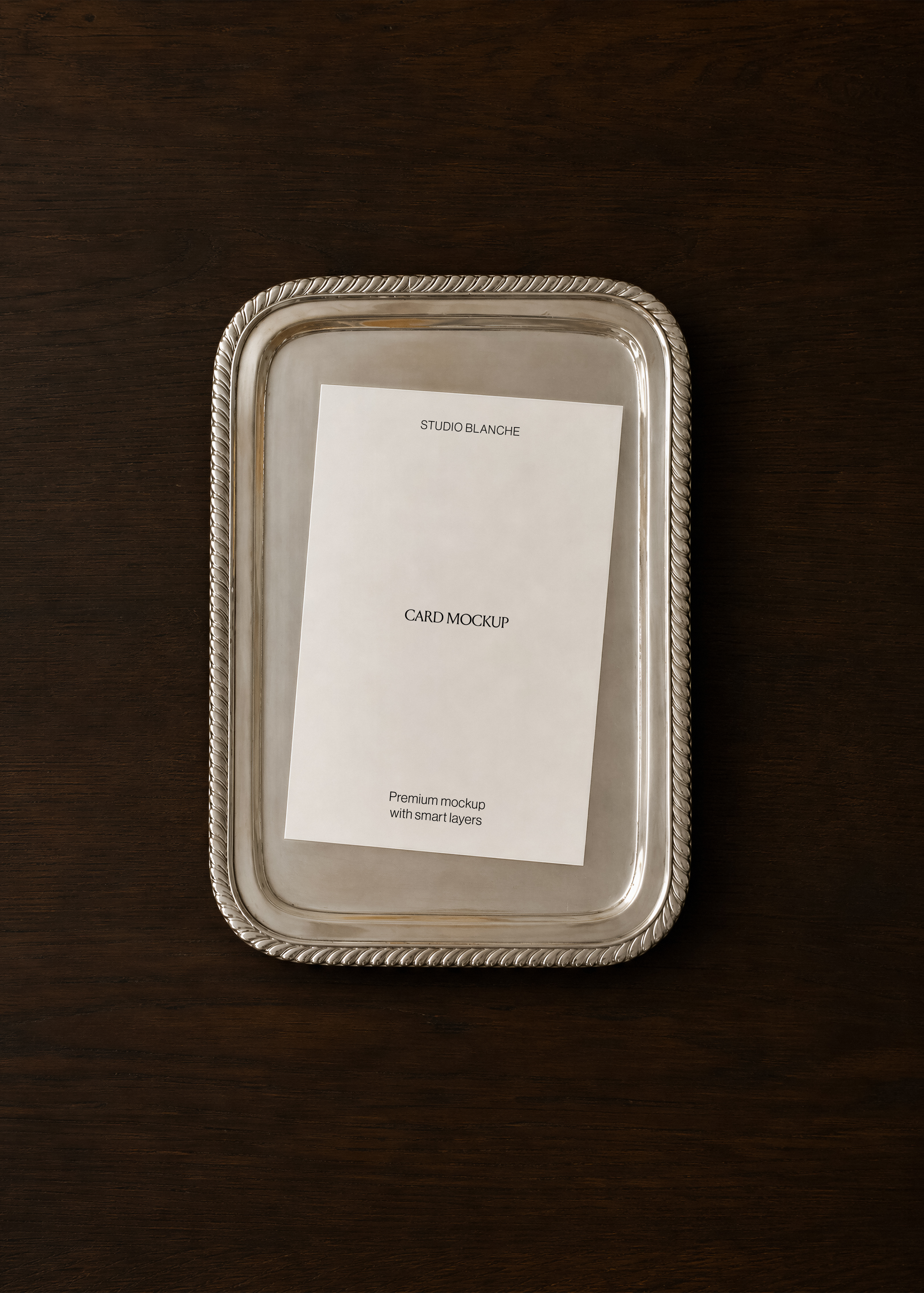 Portrait card mockup flat on polished silver rope-edged tray, dark espresso walnut surface, overhead view