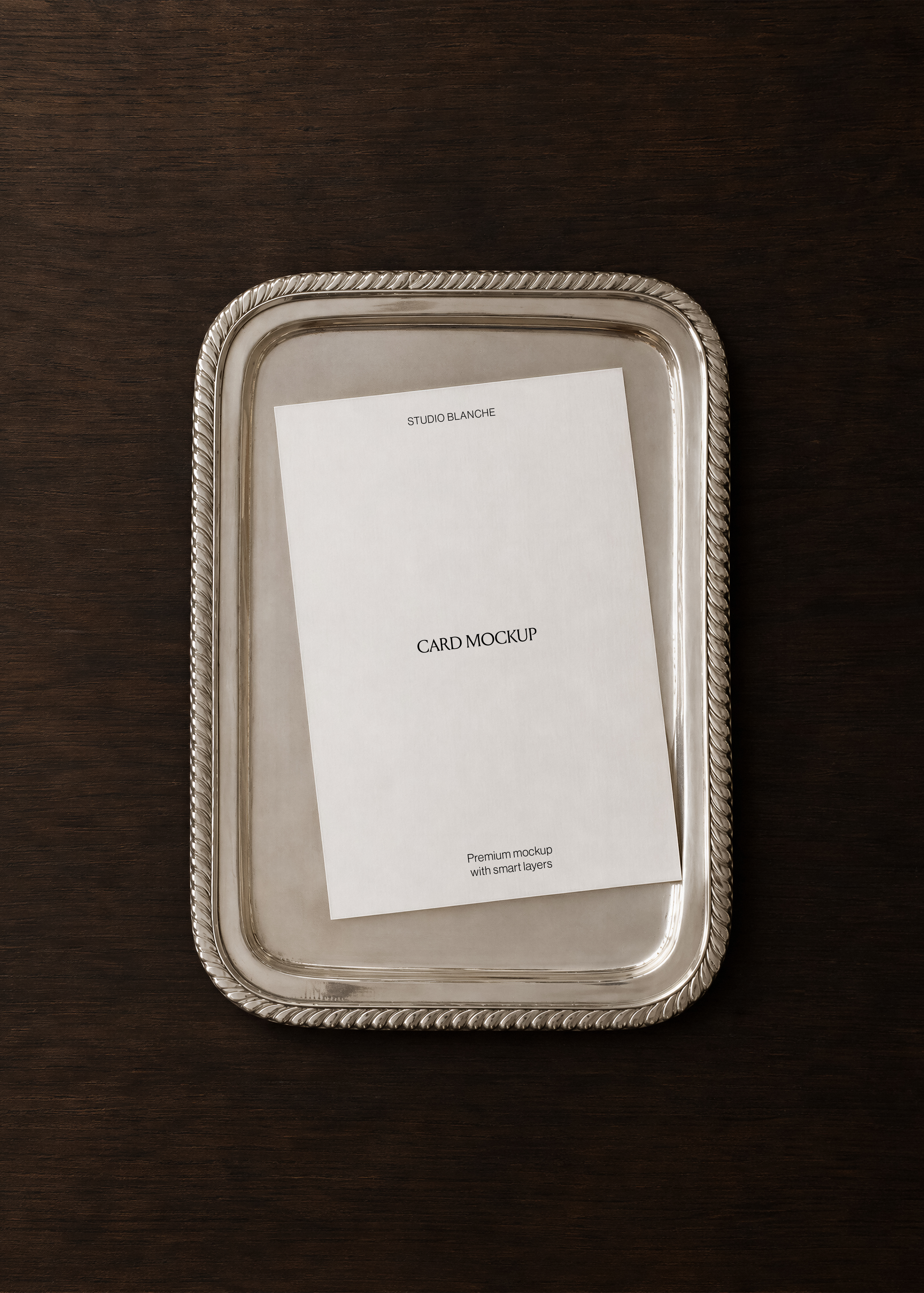 Card mockup on polished silver rope-edged tray, dark espresso walnut surface, overhead view