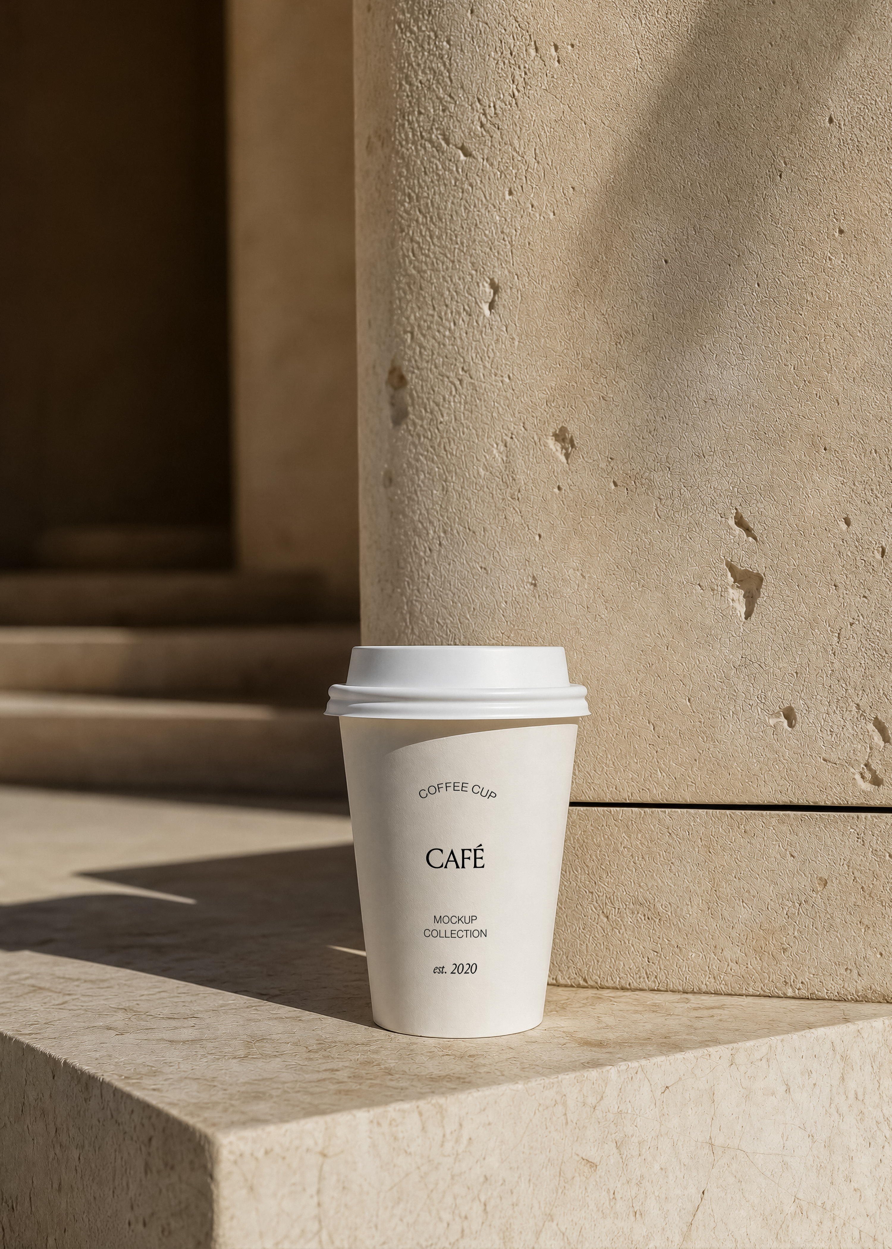 White takeaway coffee cup mockup with lid on a stone ledge against a textured sandstone wall in warm sunlight