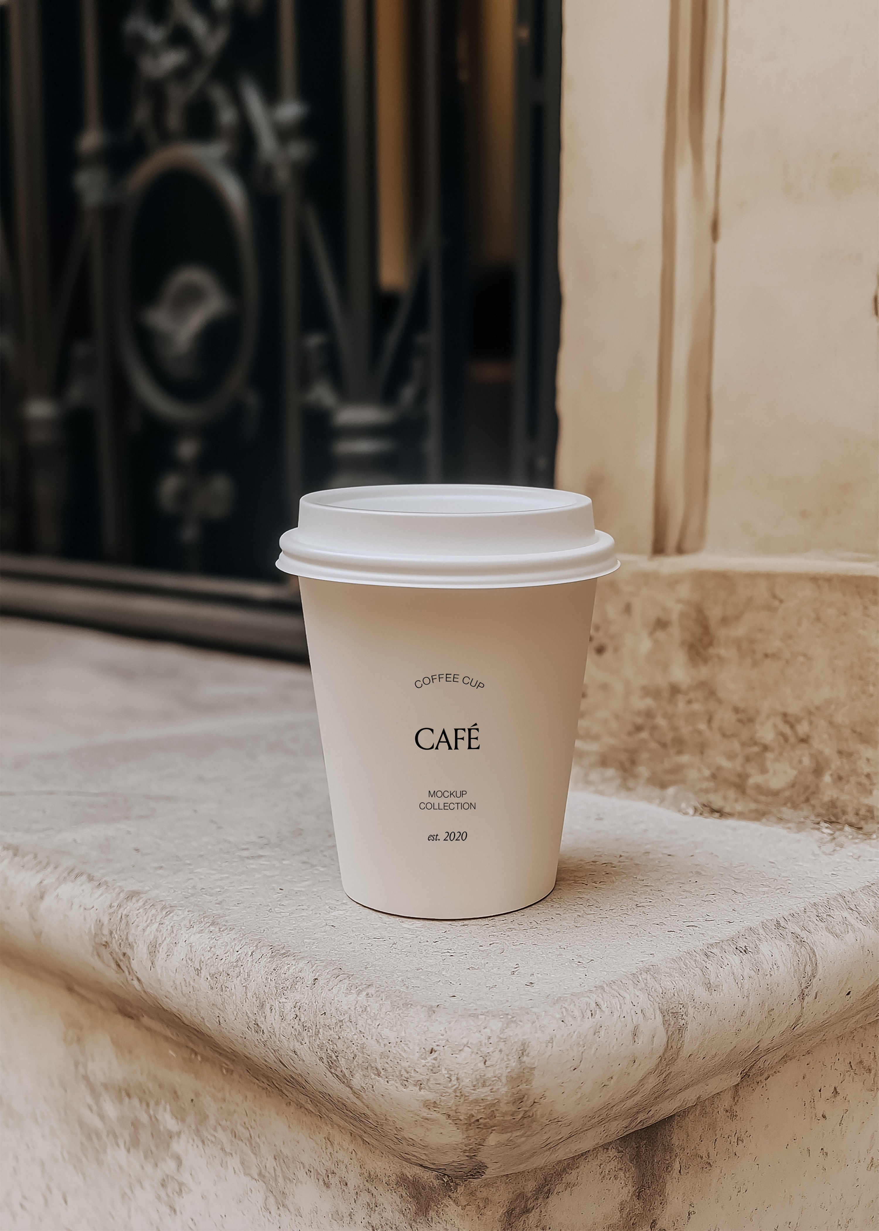 White takeaway coffee cup mockup on a weathered limestone step with a dark iron door blurred behind, warm daylight
