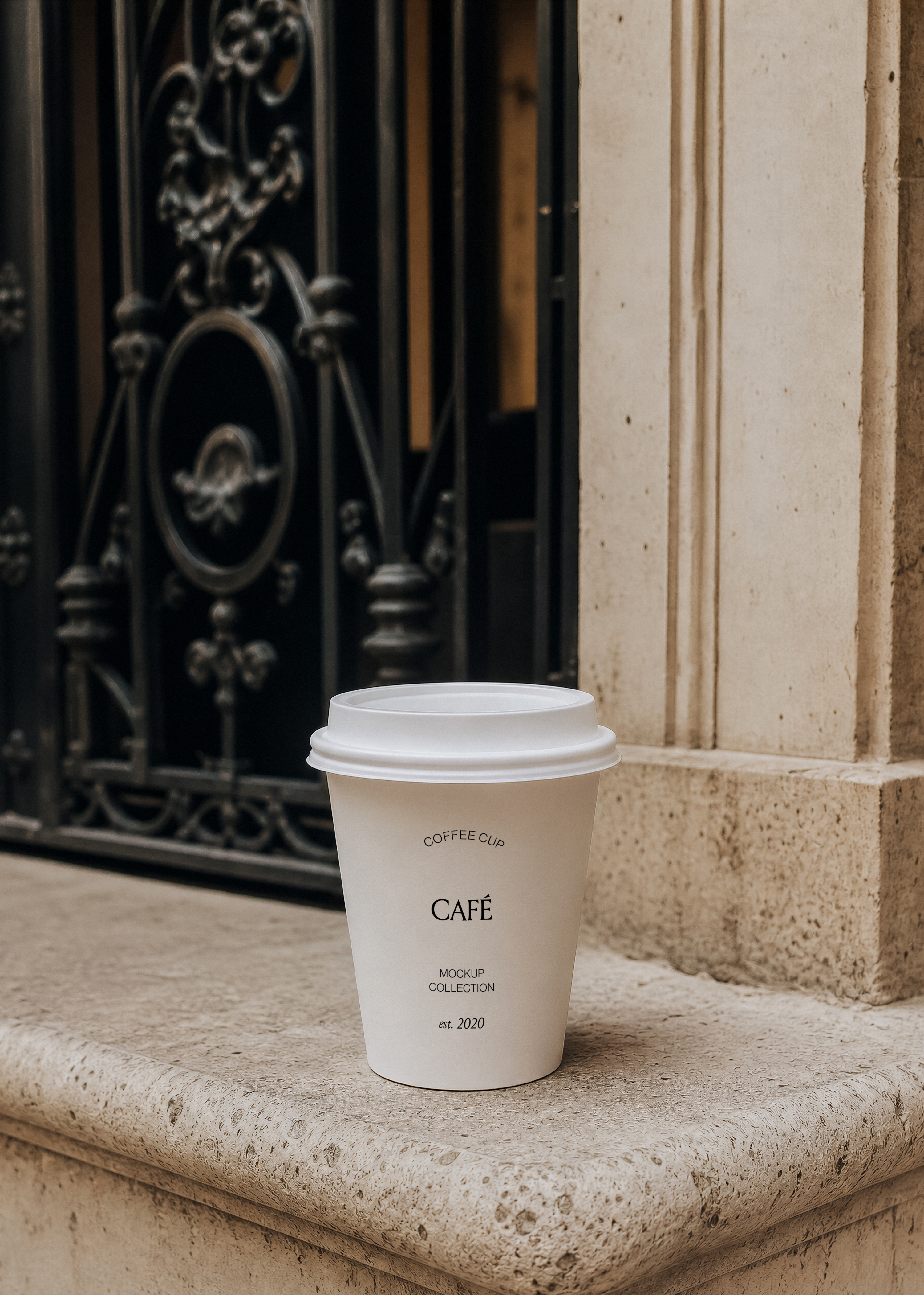 White takeaway coffee cup mockup on a weathered limestone step with a dark iron door blurred behind, warm daylight