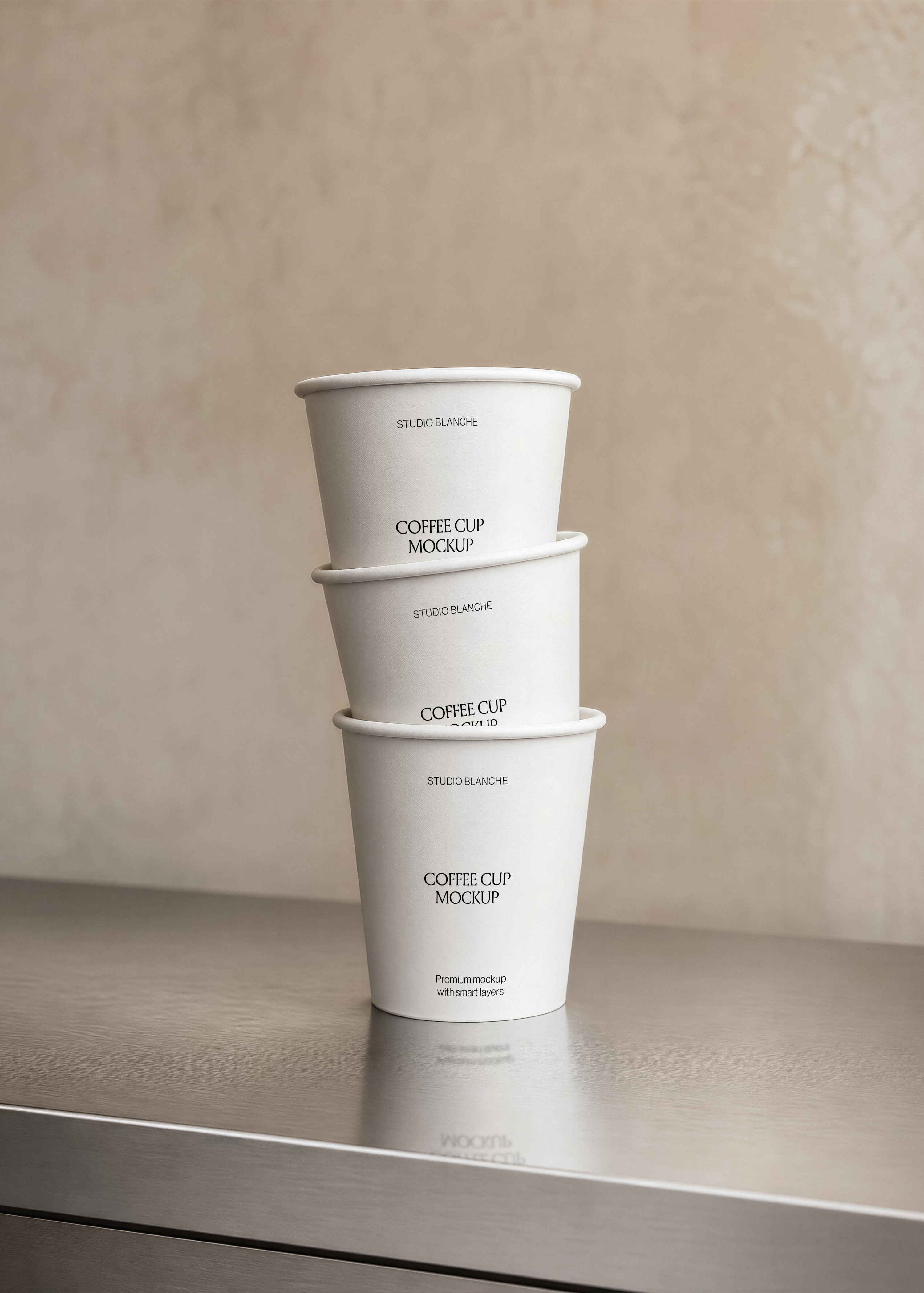 Three stacked white coffee cup mockups on brushed steel counter with soft reflection, minimal warm-toned wall backdrop