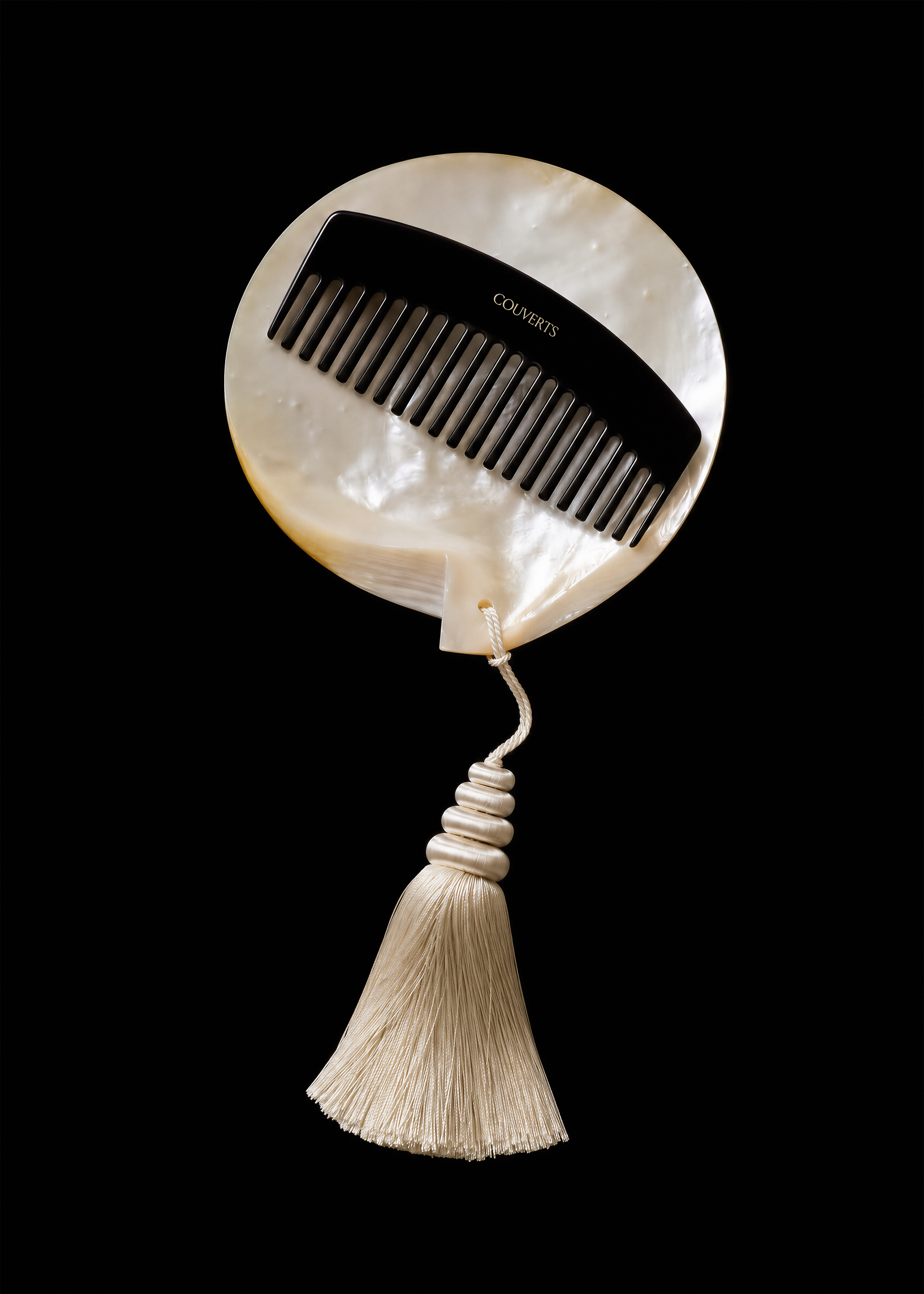 Black comb mockup with gold logo set across a round mother-of-pearl disc with cream silk tassel on black backdrop