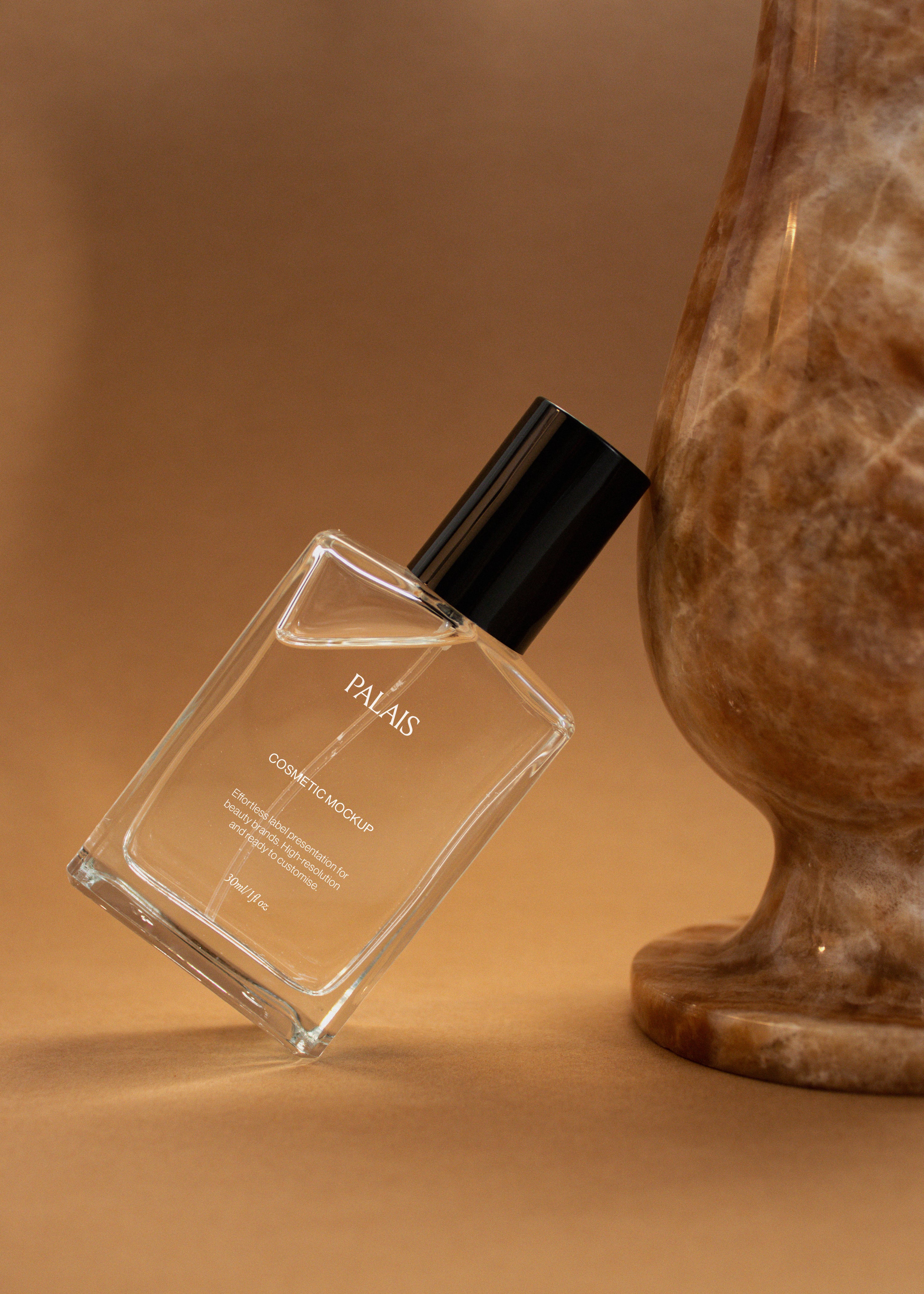 Clear glass cosmetic bottle mockup with black cap tilted against a carved brown stone form on warm caramel