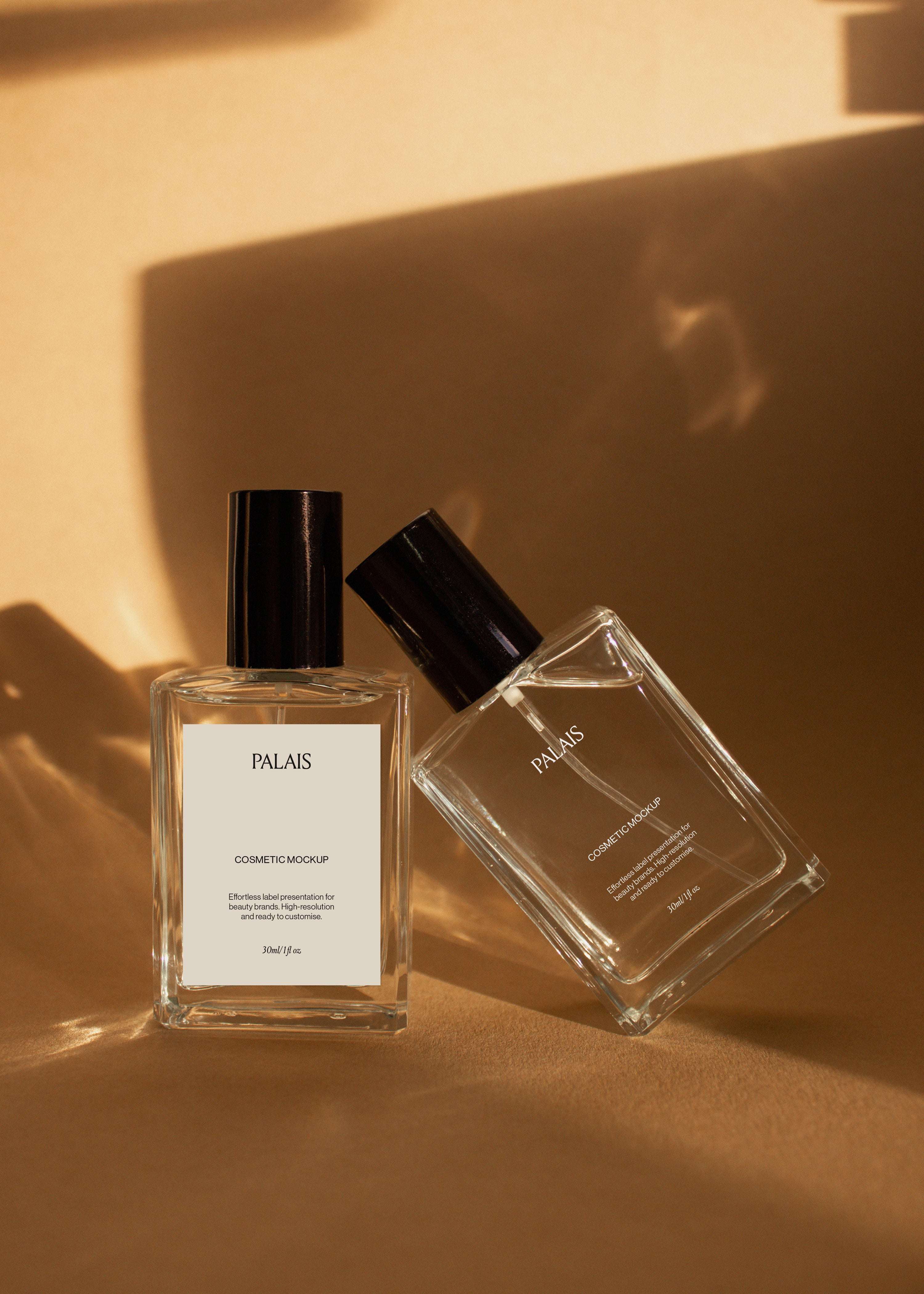 Two glass cosmetic bottle mockups with black caps on warm sandstone surface with soft directional shadows