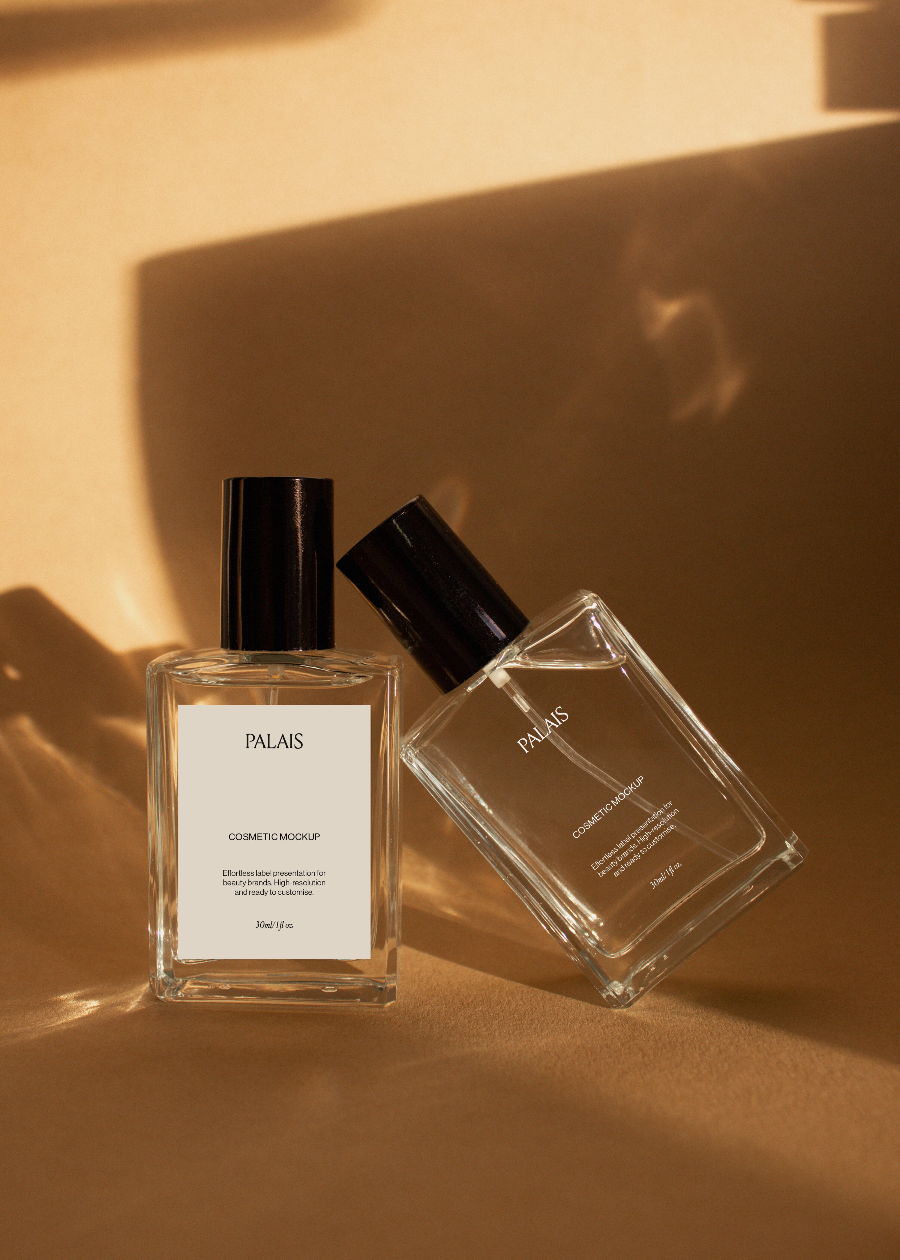 Two glass cosmetic bottle mockups with black caps on warm sandstone surface with soft directional shadows