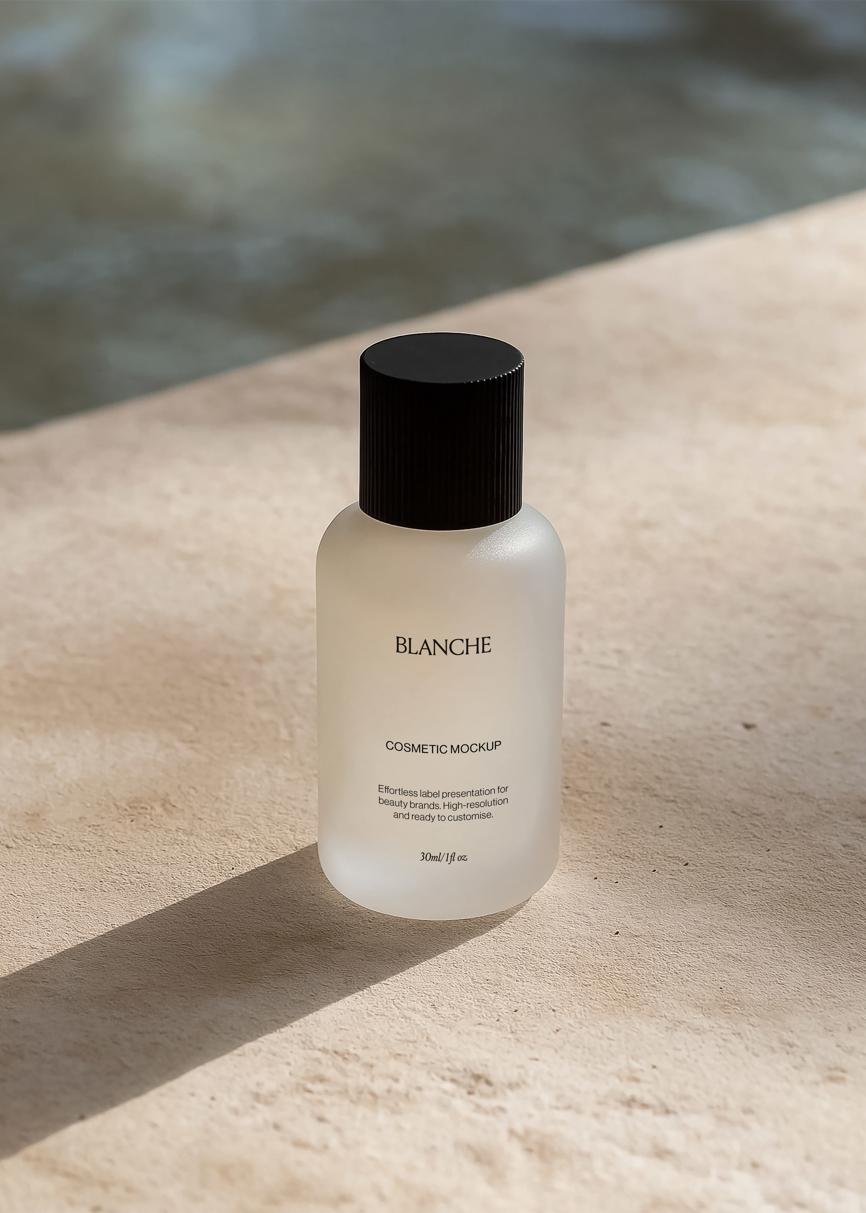 Frosted glass cosmetic bottle mockup with ribbed black cap on warm sandstone by water, long diagonal sunlight