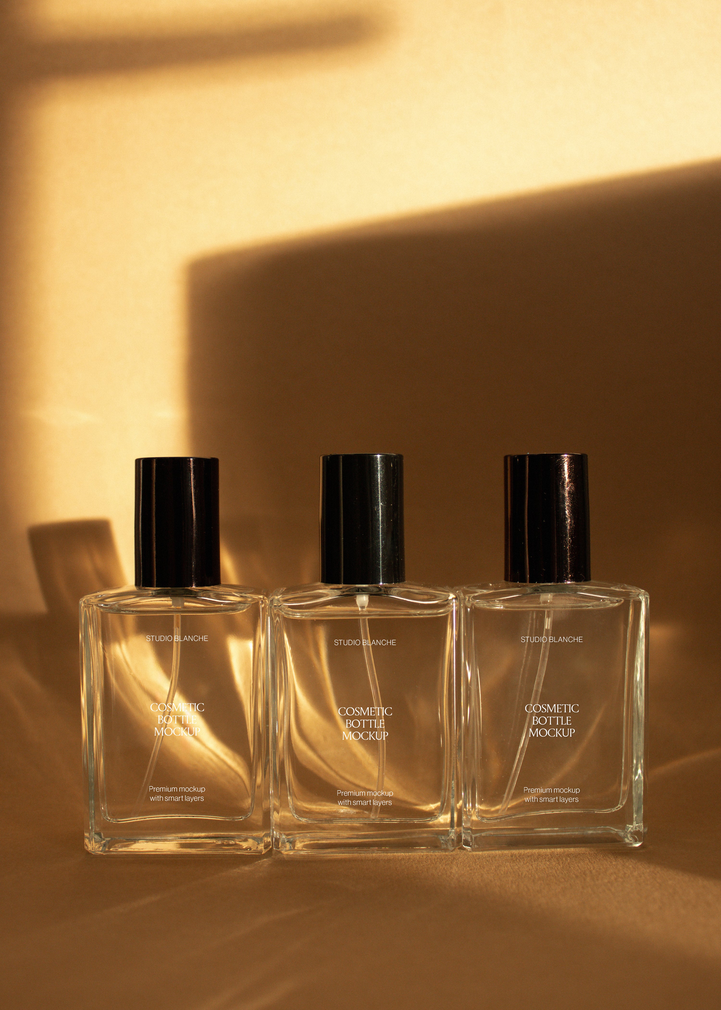 Trio of rectangular glass cosmetic bottle mockups with white, taupe and dark brown labels on sandstone backdrop