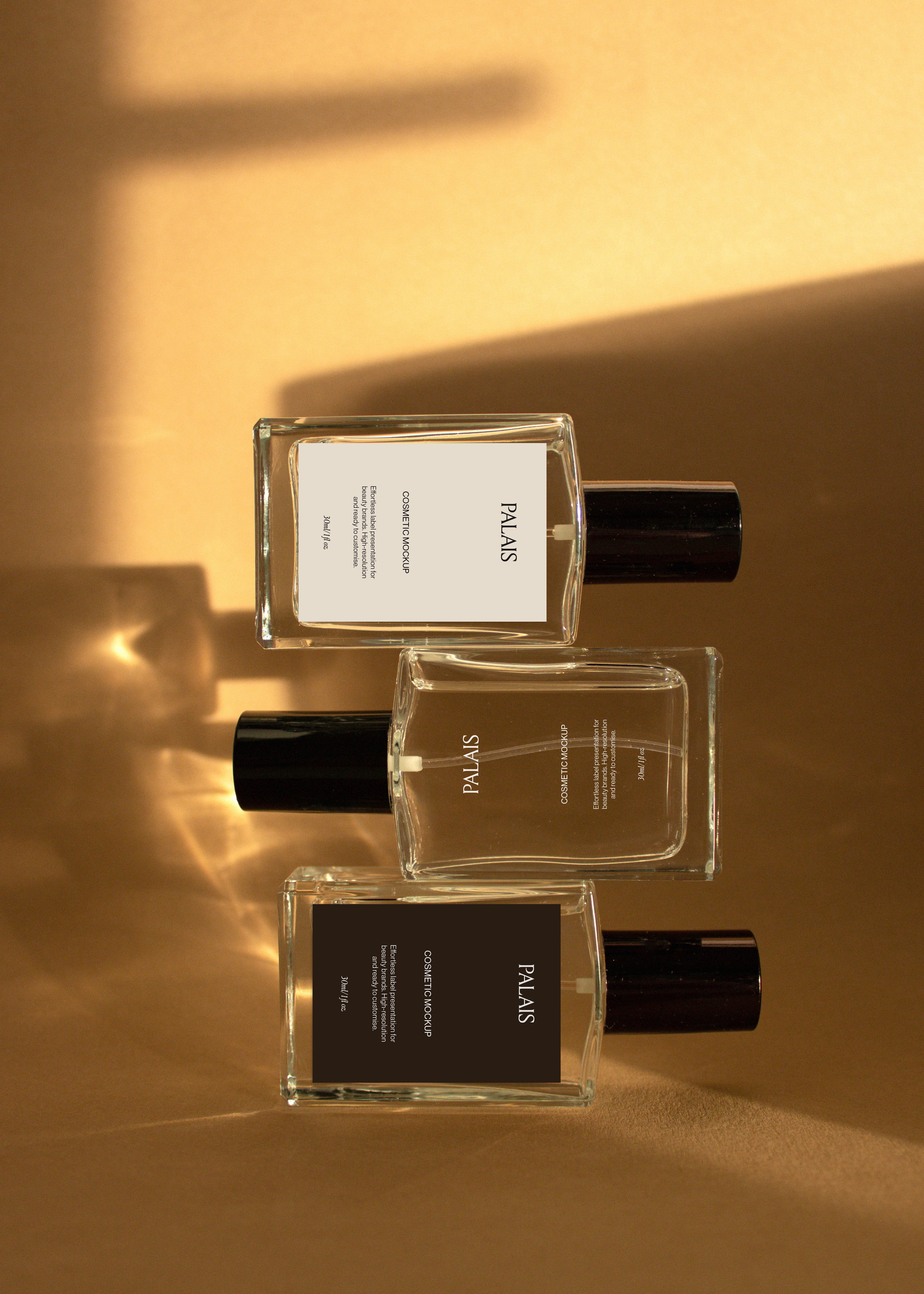 Three glass cosmetic bottle mockups lying flat in a staggered row on warm sandstone surface, editorial flat-lay