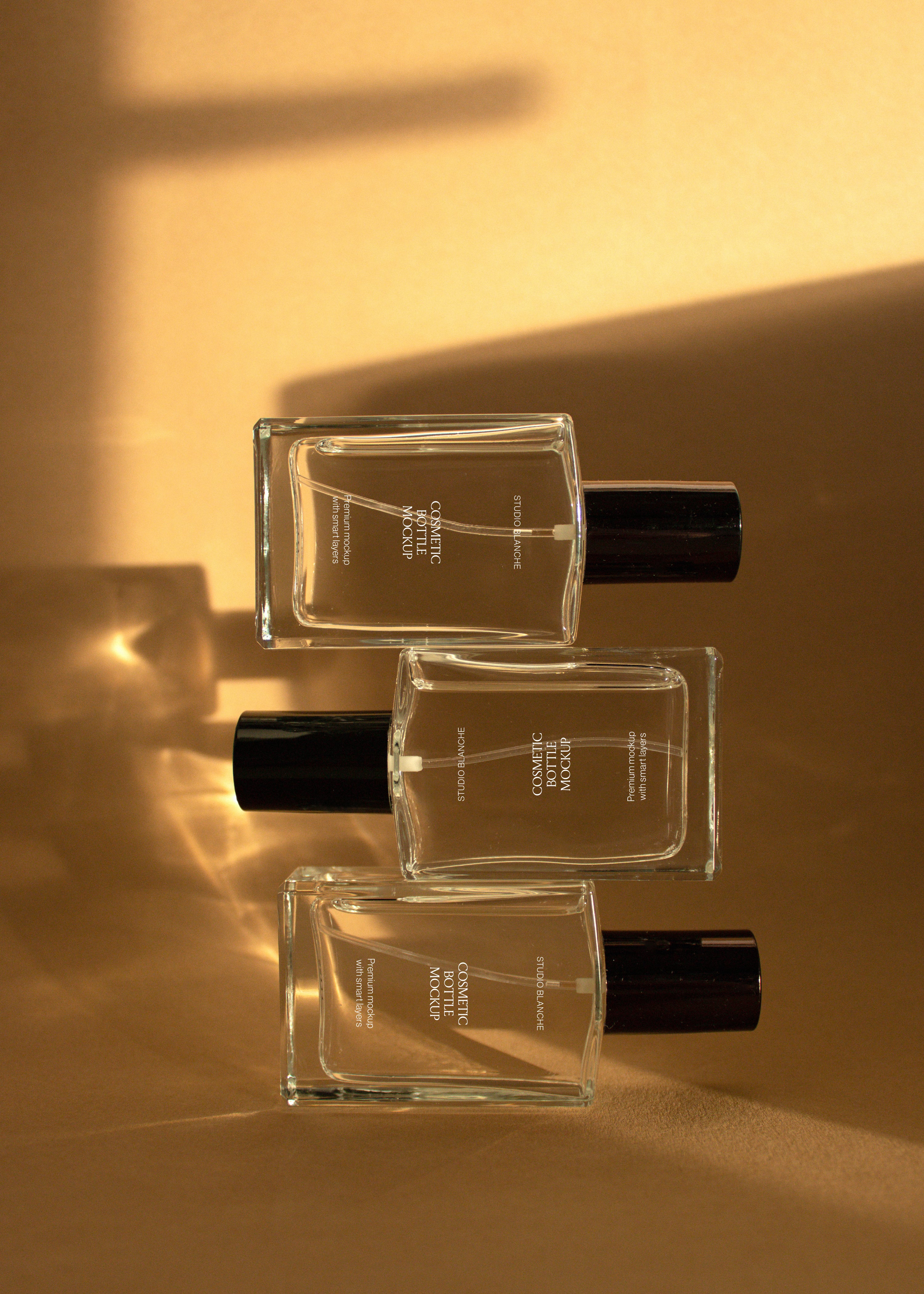 Trio of clear glass cosmetic bottle mockups with white, taupe and dark brown labels flat on sandstone backdrop