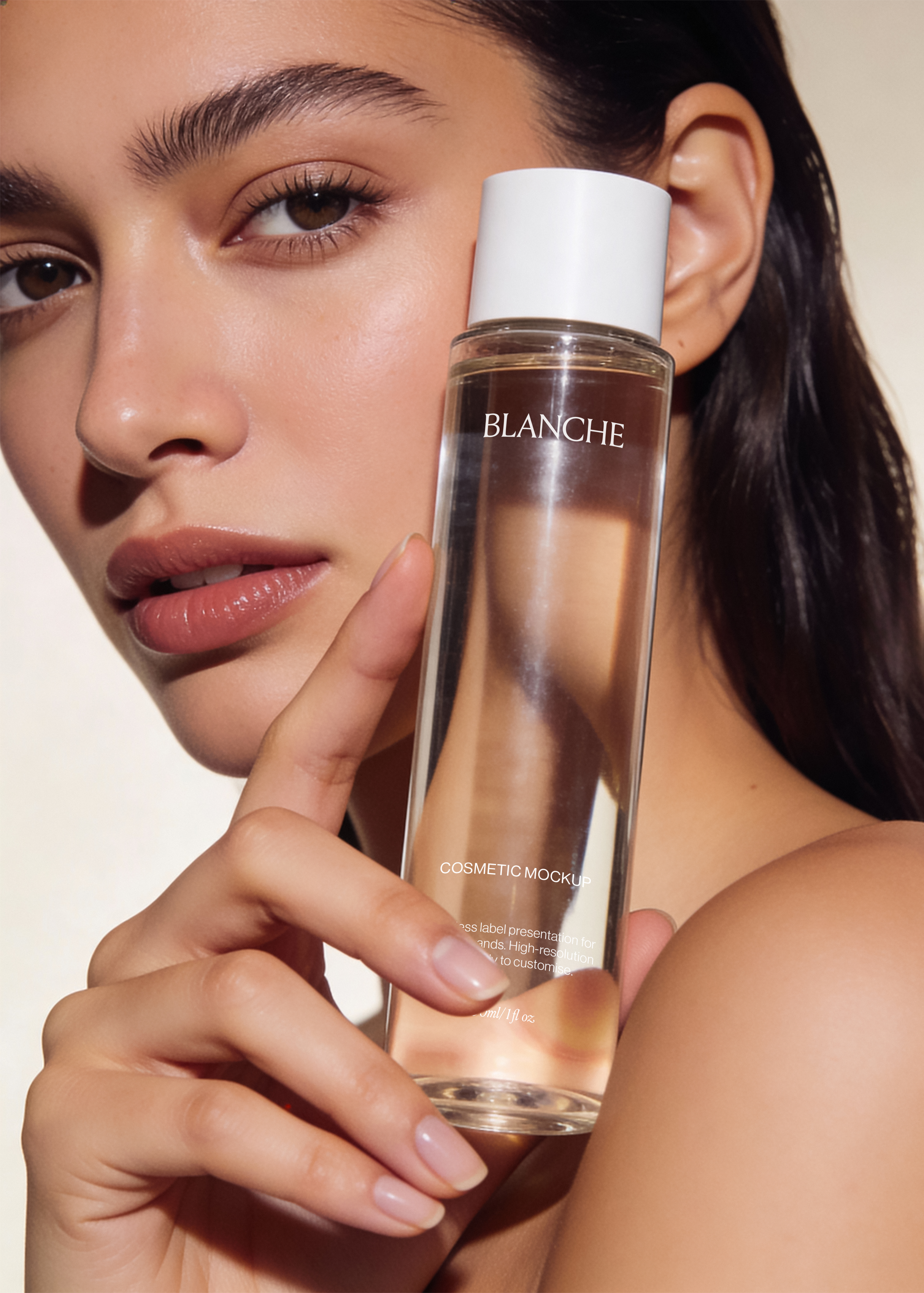 Clear glass cosmetic bottle mockup with white cap held against a model's cheek in a warm, close-cropped beauty scene