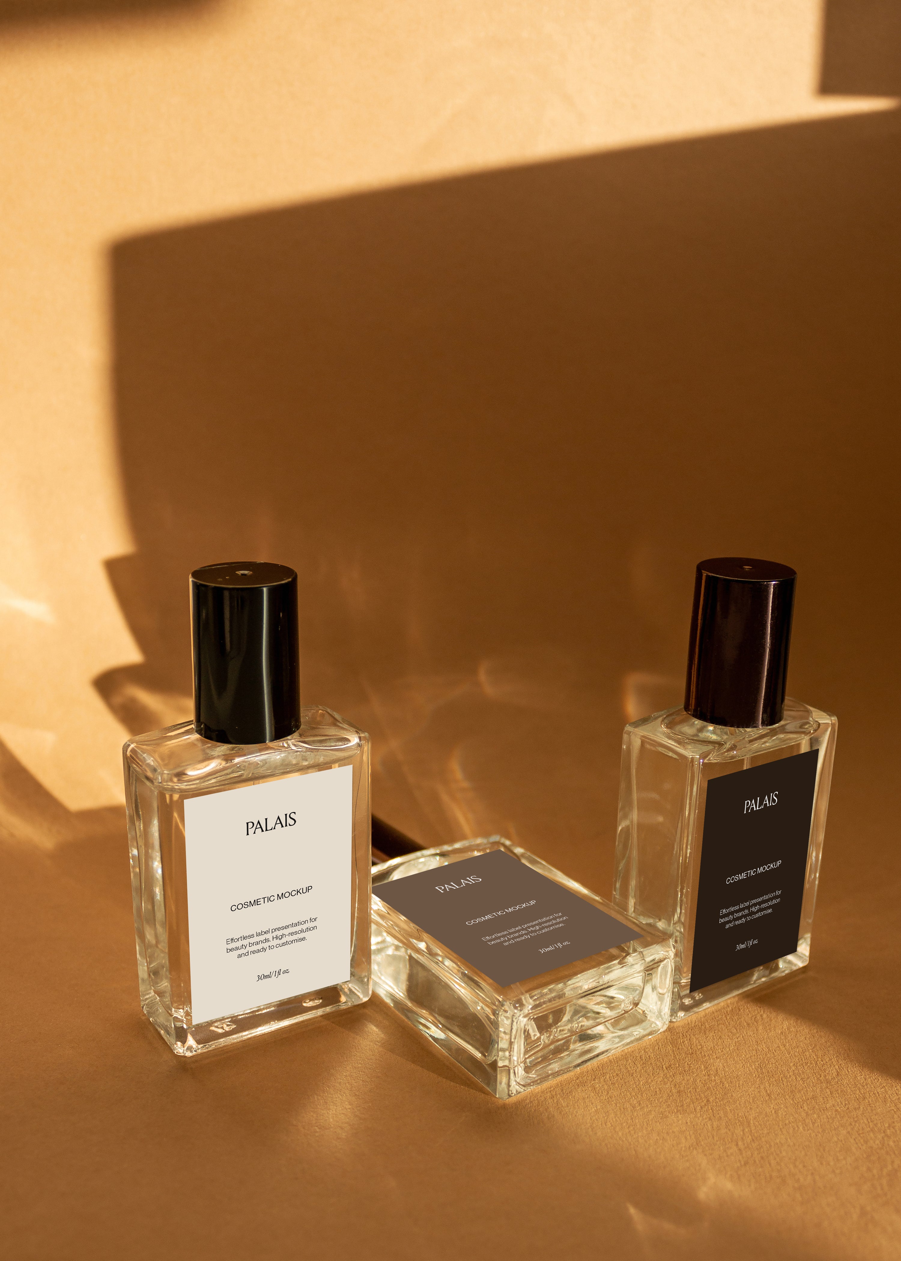 Two upright glass cosmetic bottle mockups with black caps and one lying flat between them on warm sandstone