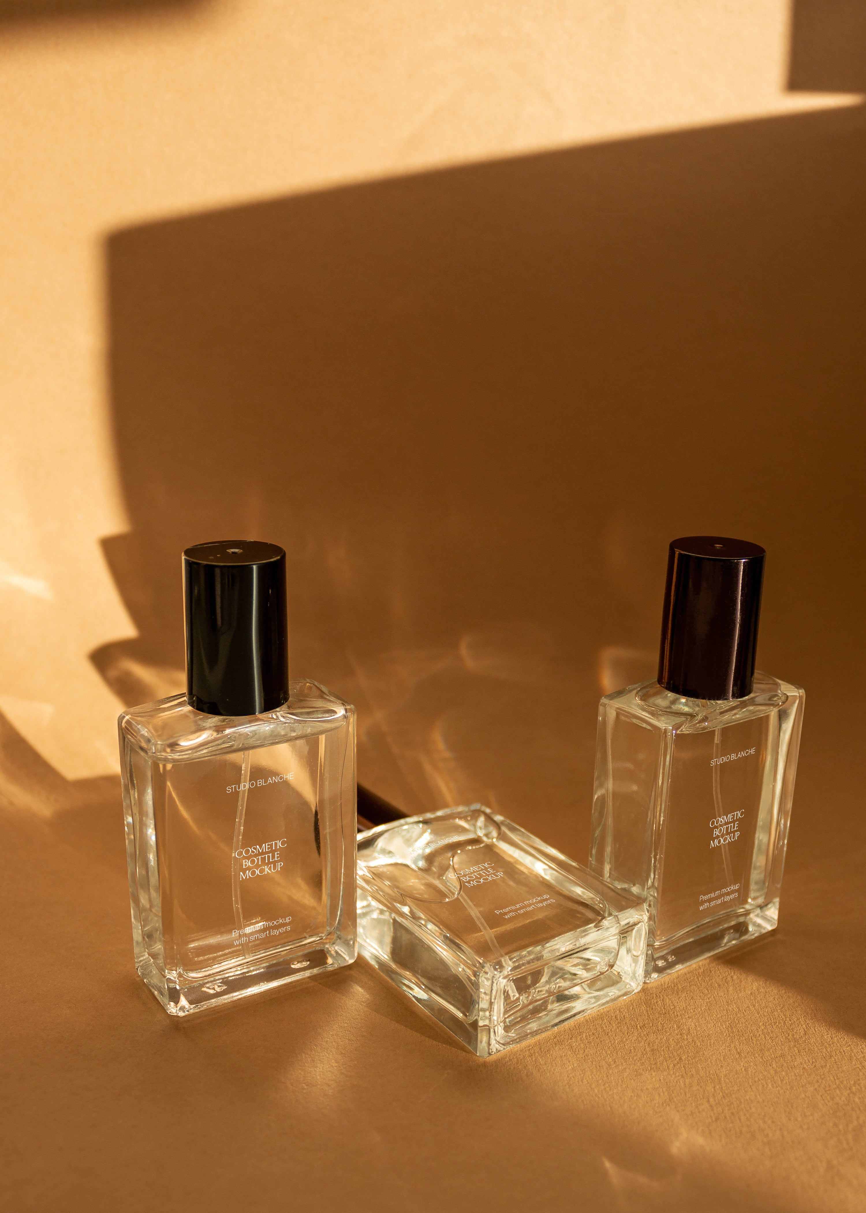 Trio of clear glass cosmetic bottle mockups with white, taupe and dark labels on warm sandstone surface