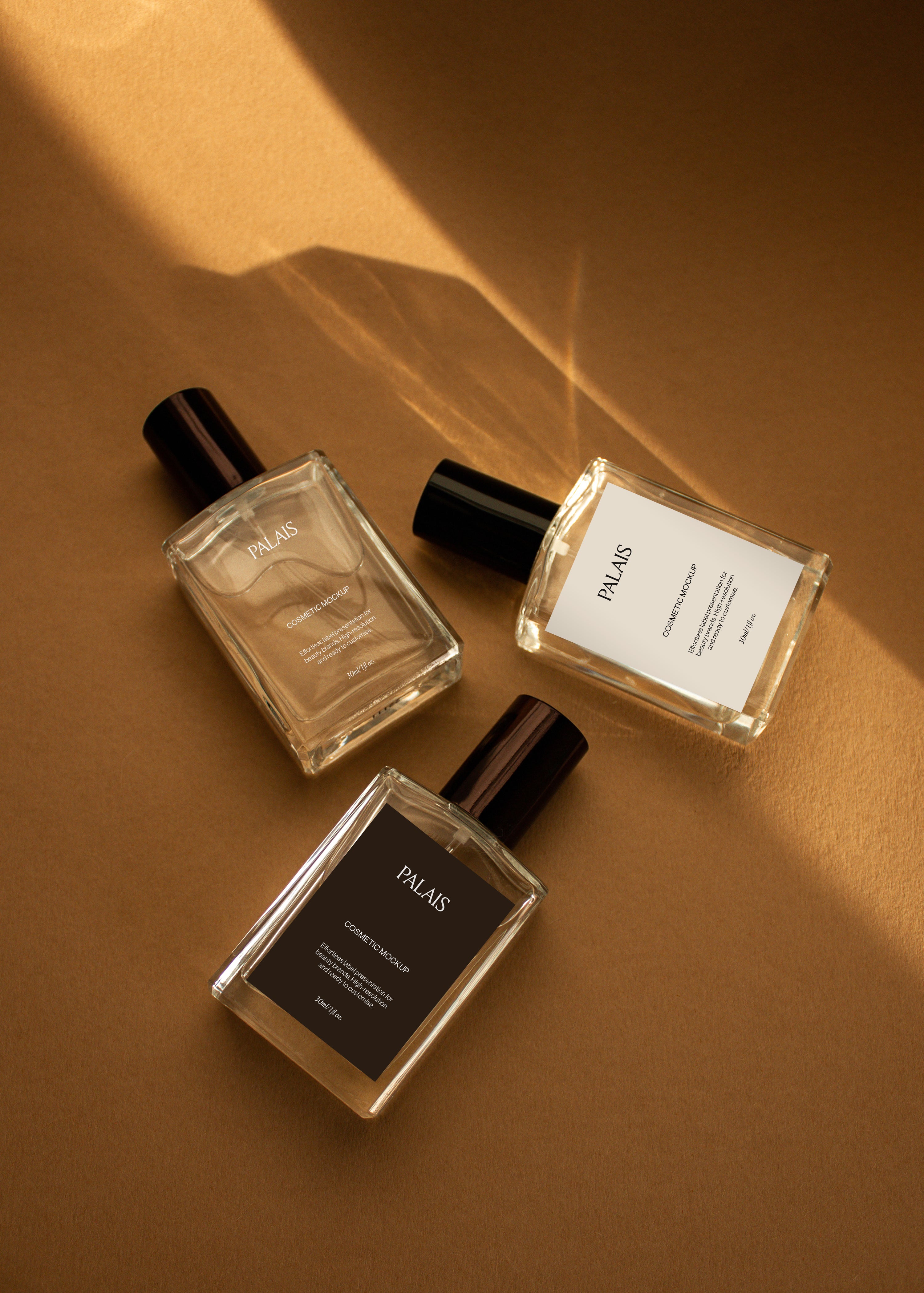 Three glass cosmetic bottle mockups with black caps arranged at angles on warm sandstone surface, overhead view