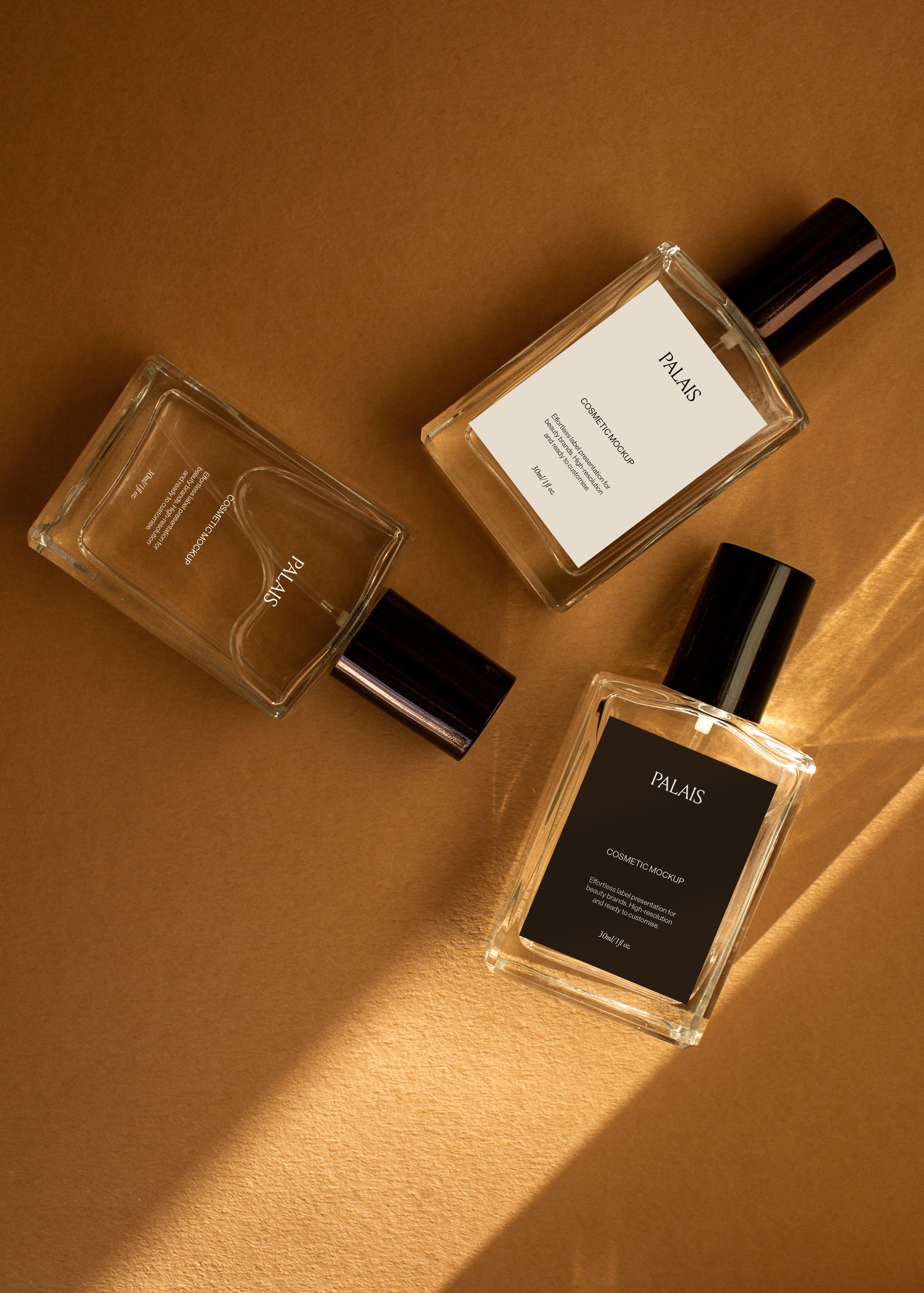 Three glass cosmetic bottle mockups with black caps turned in different directions on warm sandstone in sunlight