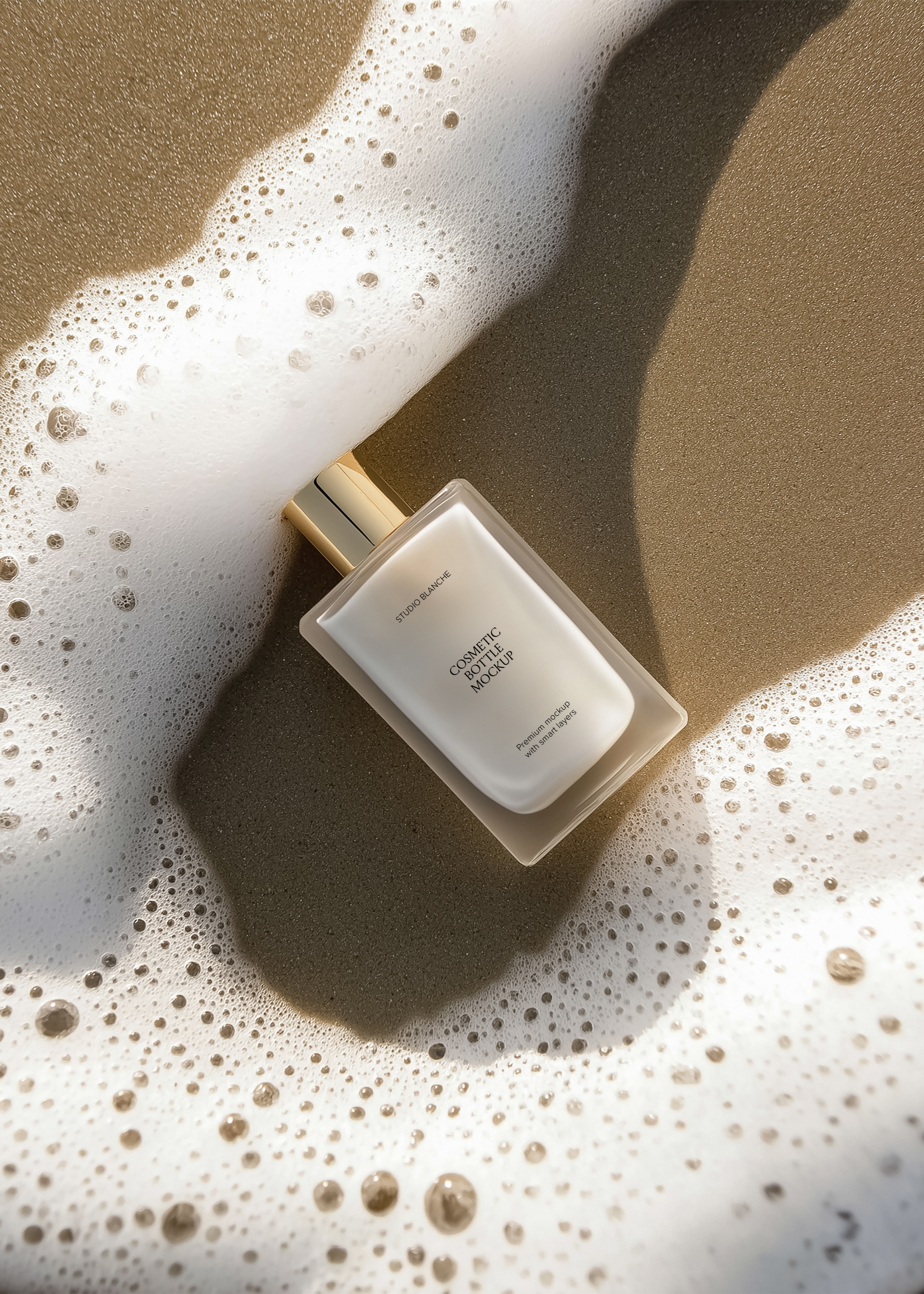 Frosted white cosmetic bottle with gold cap on sandy surface with sea foam wash, overhead flatlay, editorial product mockup