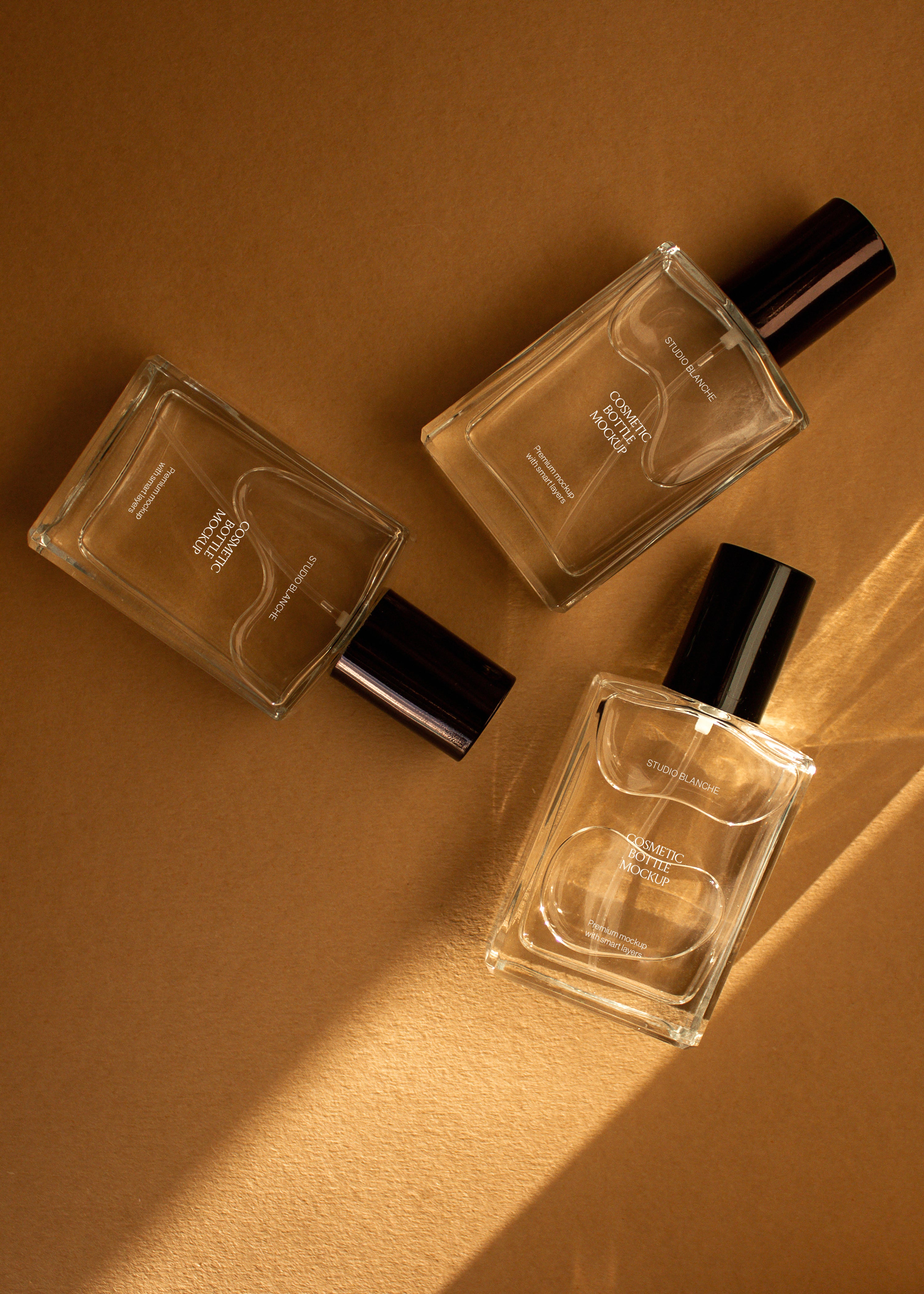 Trio of clear glass cosmetic bottle mockups with white and dark labels on warm sandstone with a diagonal light shaft