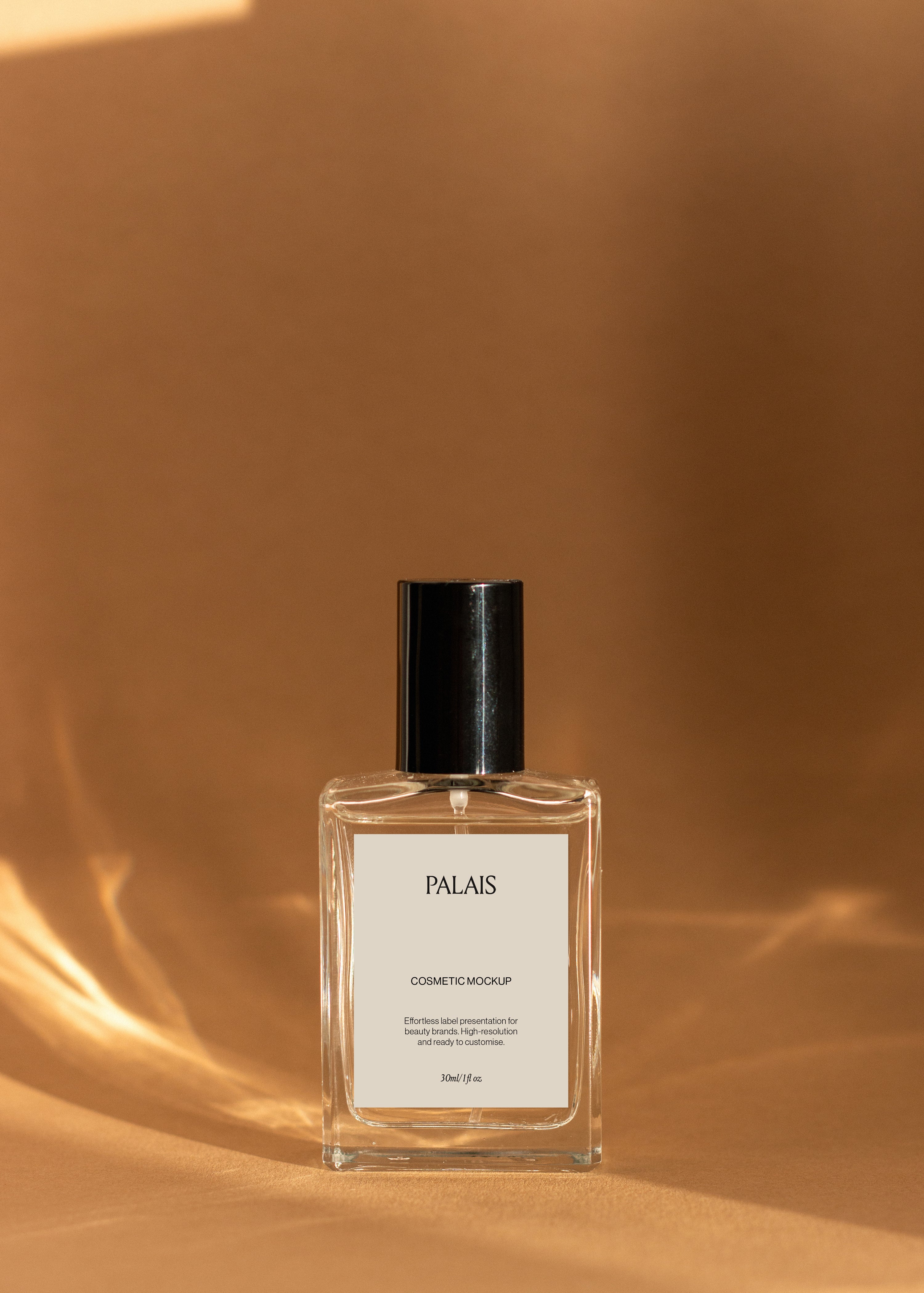 Single upright glass cosmetic bottle mockup with black cap and white label on warm sandstone with draped fabric