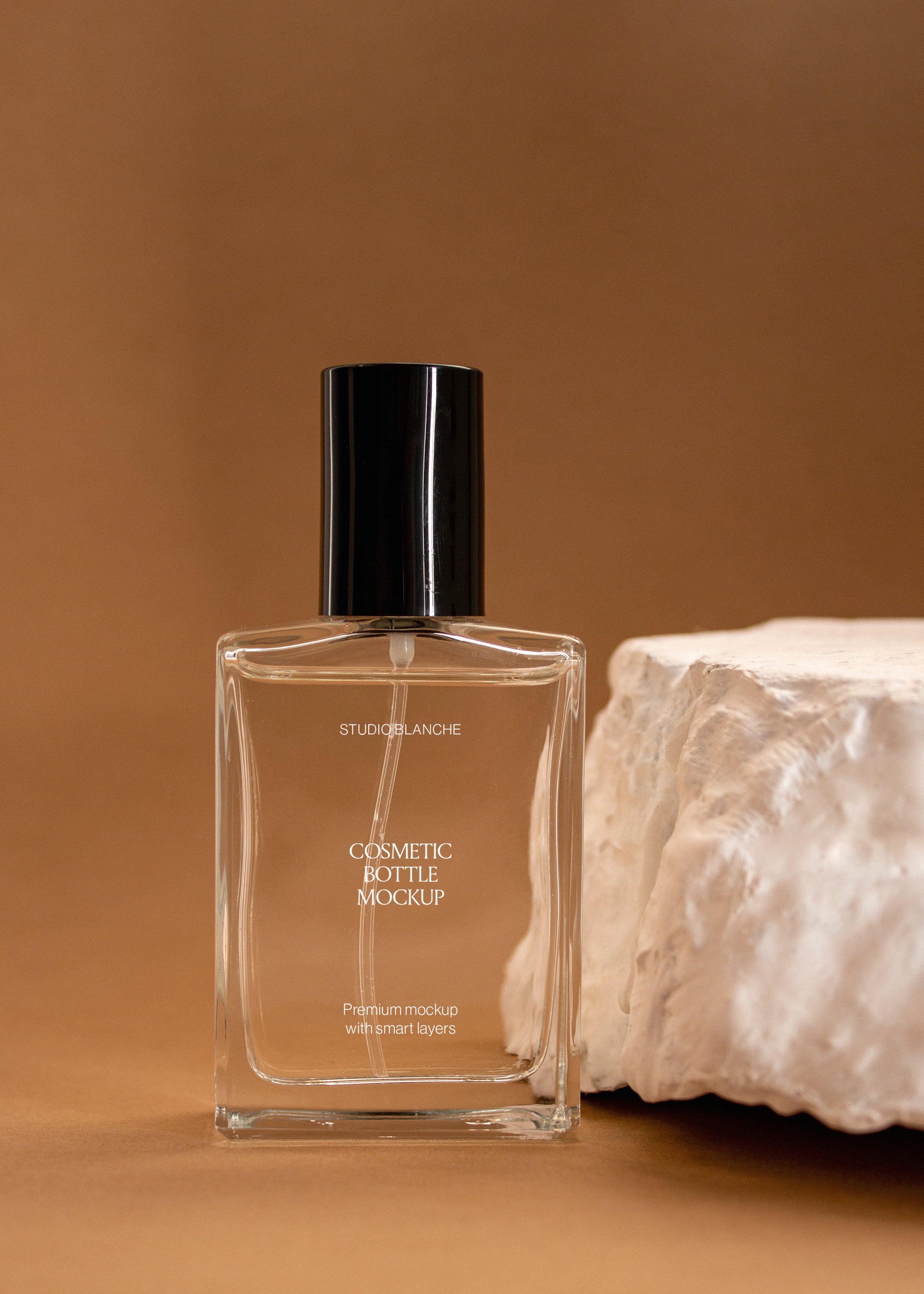 Clear glass cosmetic bottle mockup with black spray cap and white label next to raw stone on warm caramel backdrop
