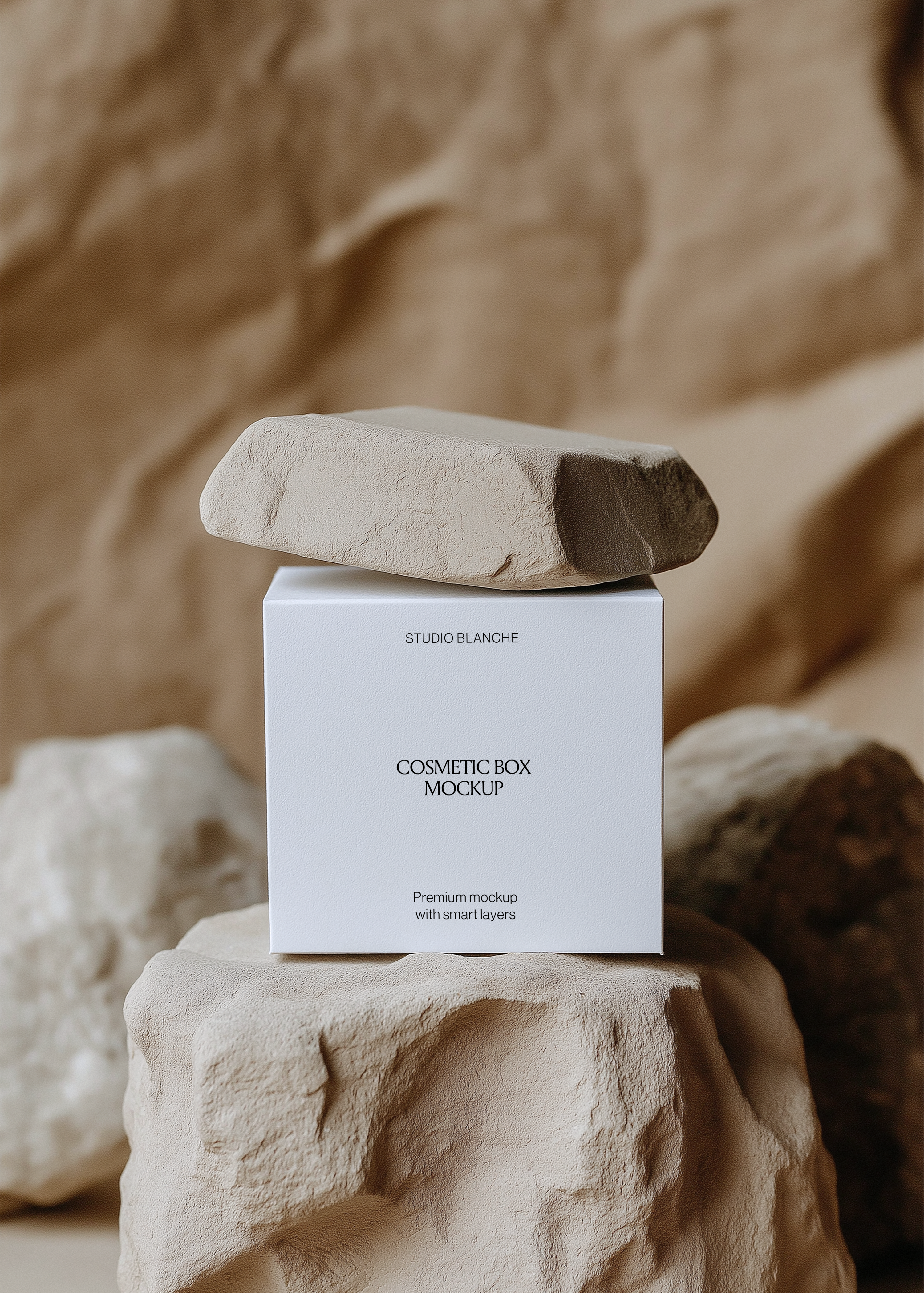 Front view of a white cosmetic box mockup reading Studio Blanche on a beige rock among stones in soft warm tones