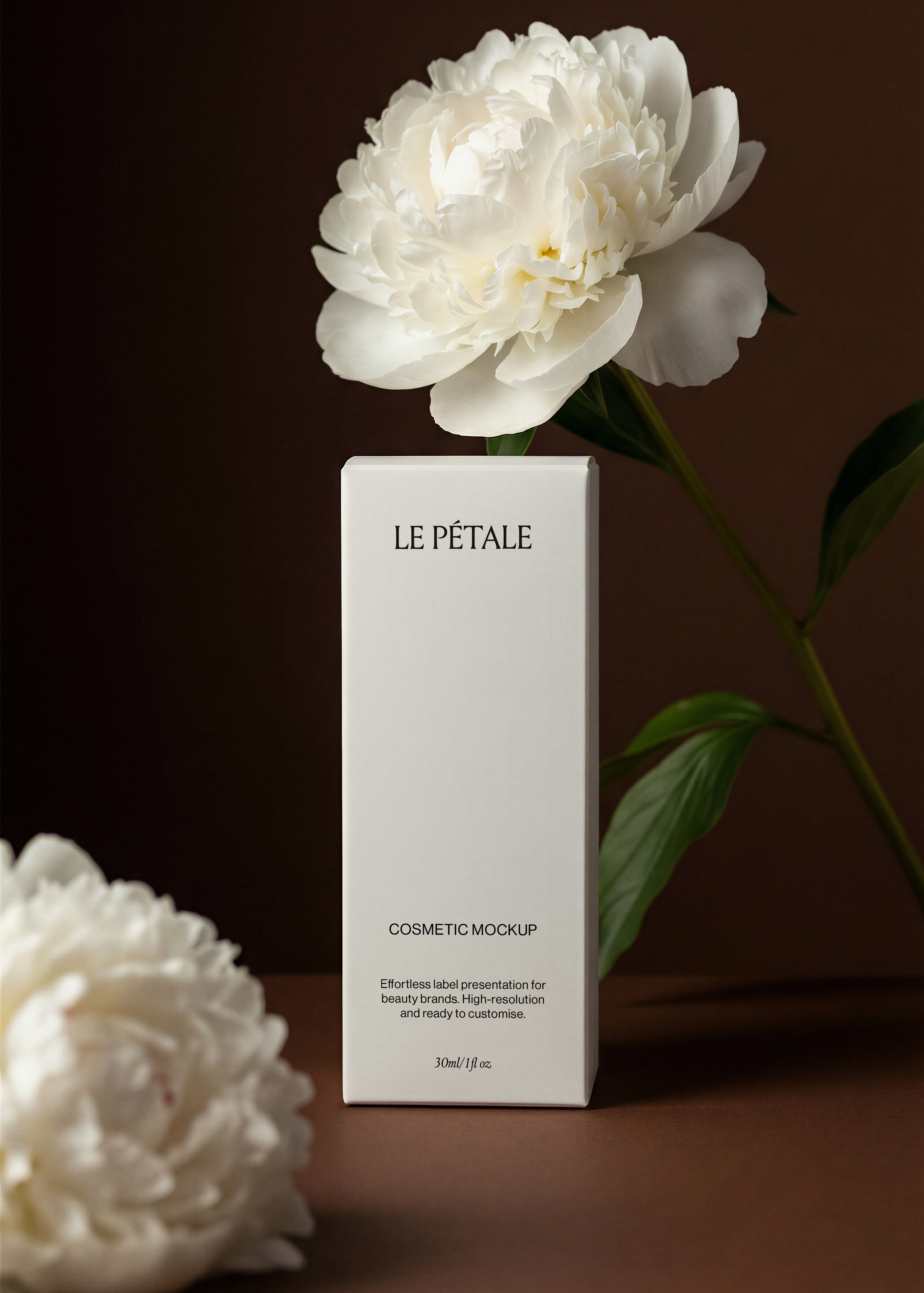 Tall white cosmetic box mockup with printed label, full white peony overhead, second peony foreground left, deep espresso backdrop