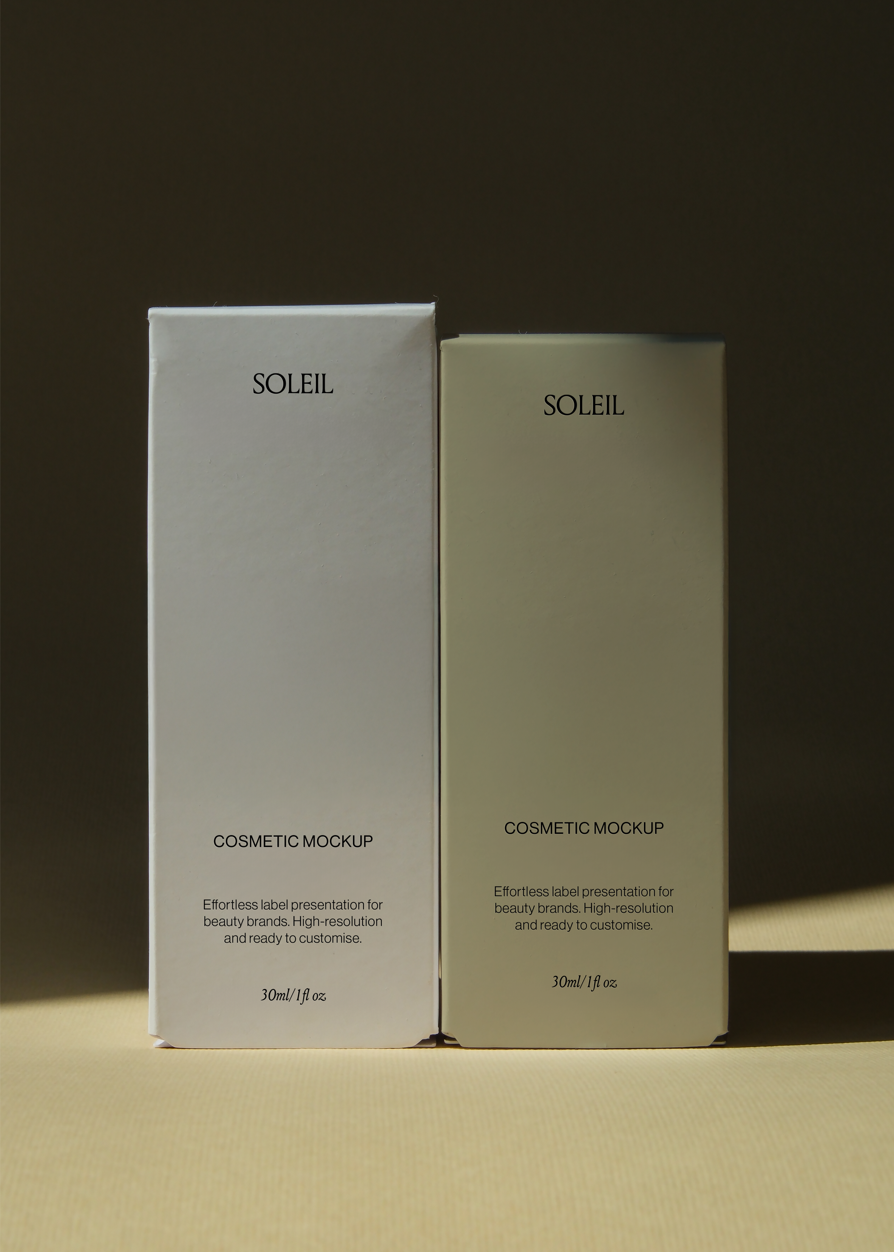 Two tall cosmetic boxes standing side by side on sand-toned surface against dark backdrop, warm side lighting, editorial mood