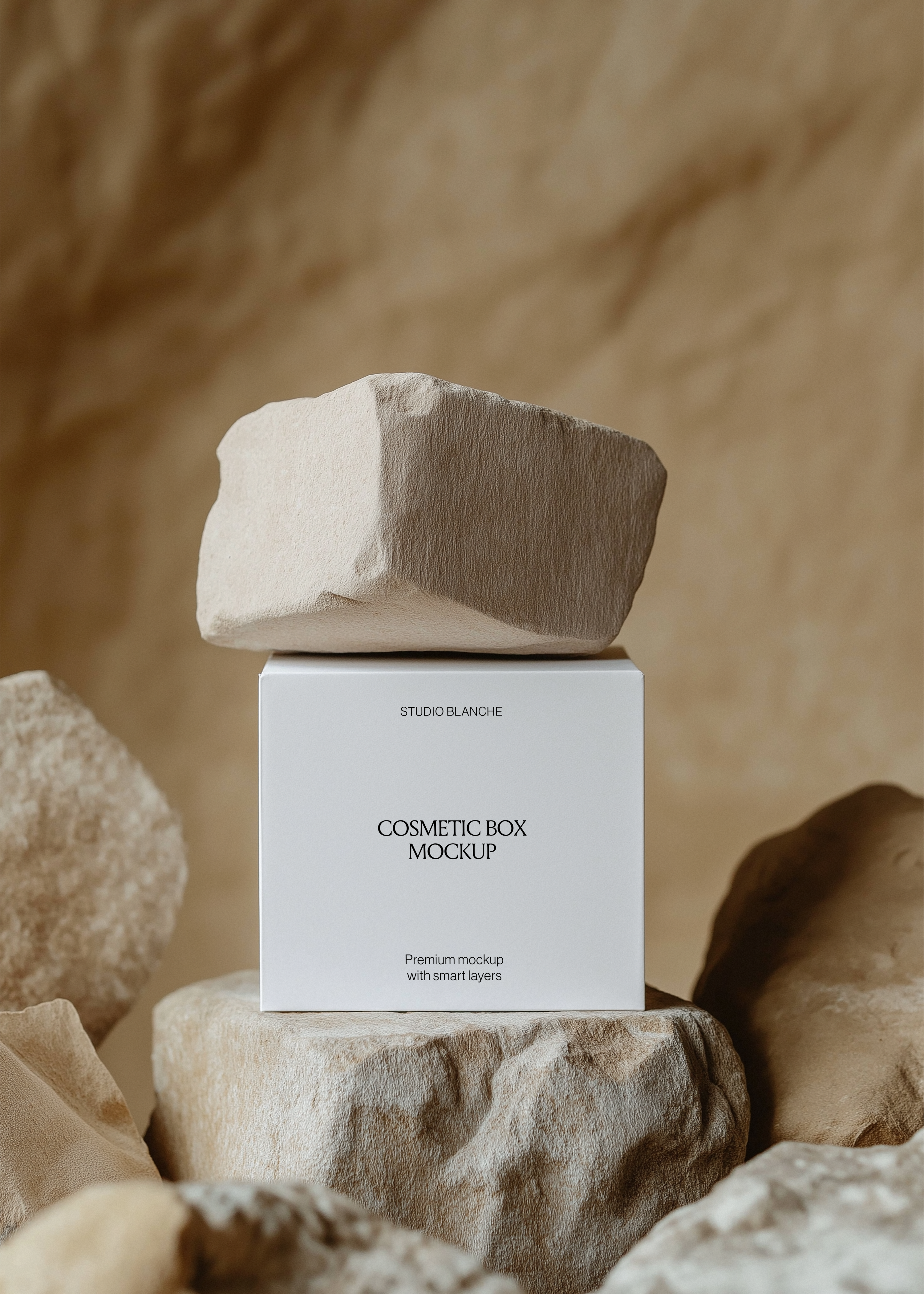 Front view of a white cosmetic box mockup reading Studio Blanche balanced on sandstone rocks in a warm neutral setting