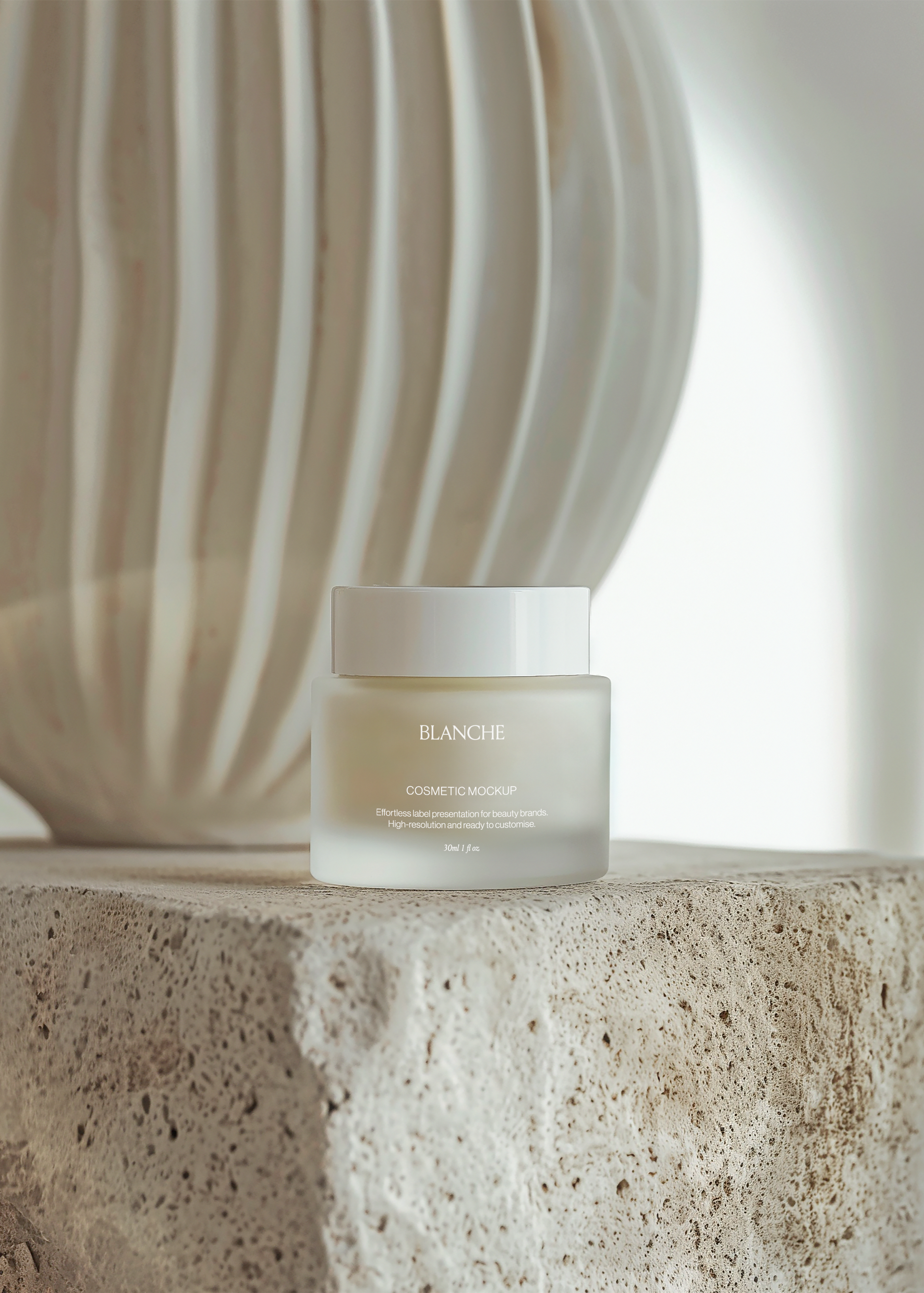 Frosted glass cosmetic jar mockup with white lid on rough travertine block, fluted ceramic vase blurred behind