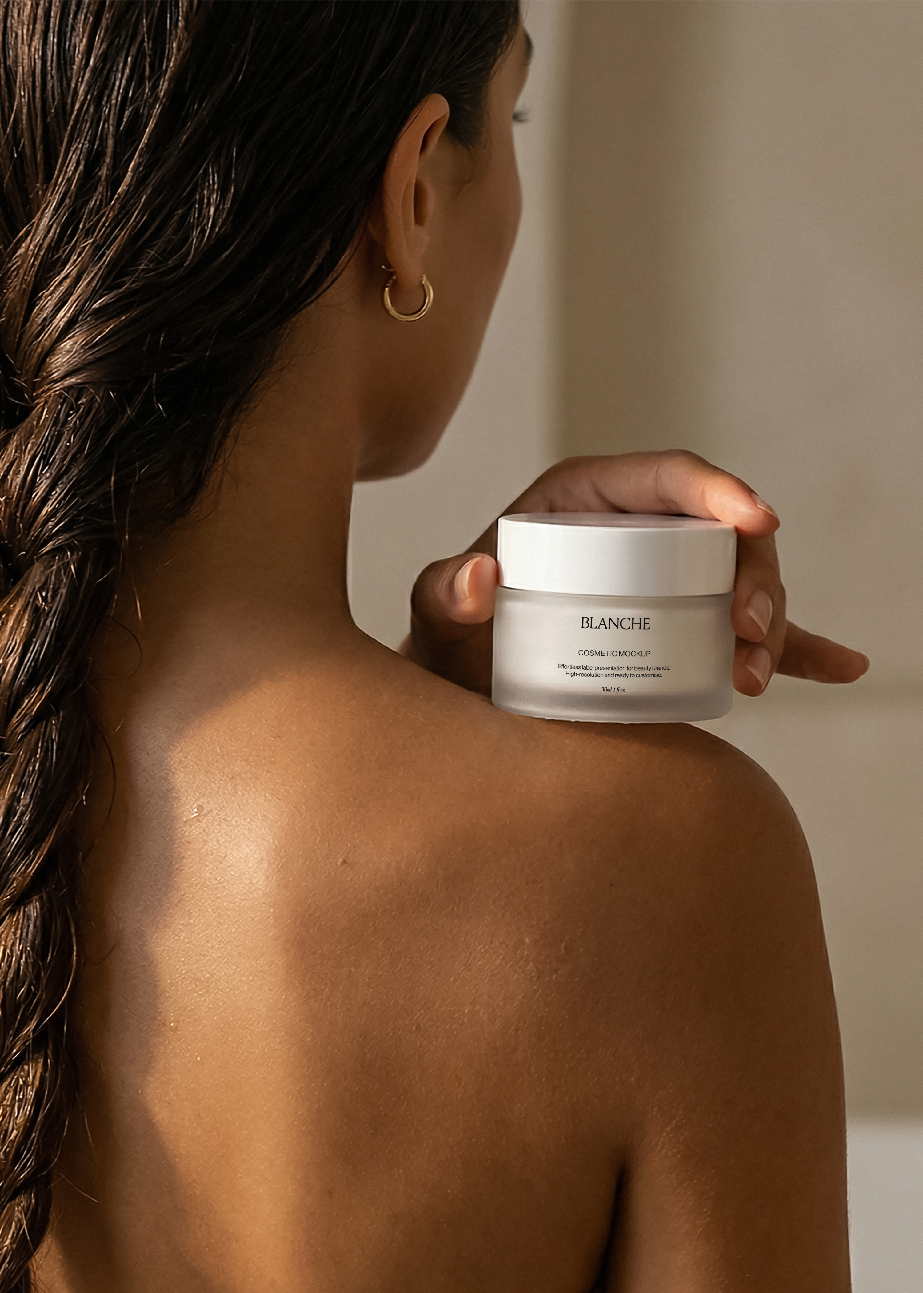 Frosted cosmetic jar mockup with white lid held against a bare shoulder in warm light, intimate editorial styling