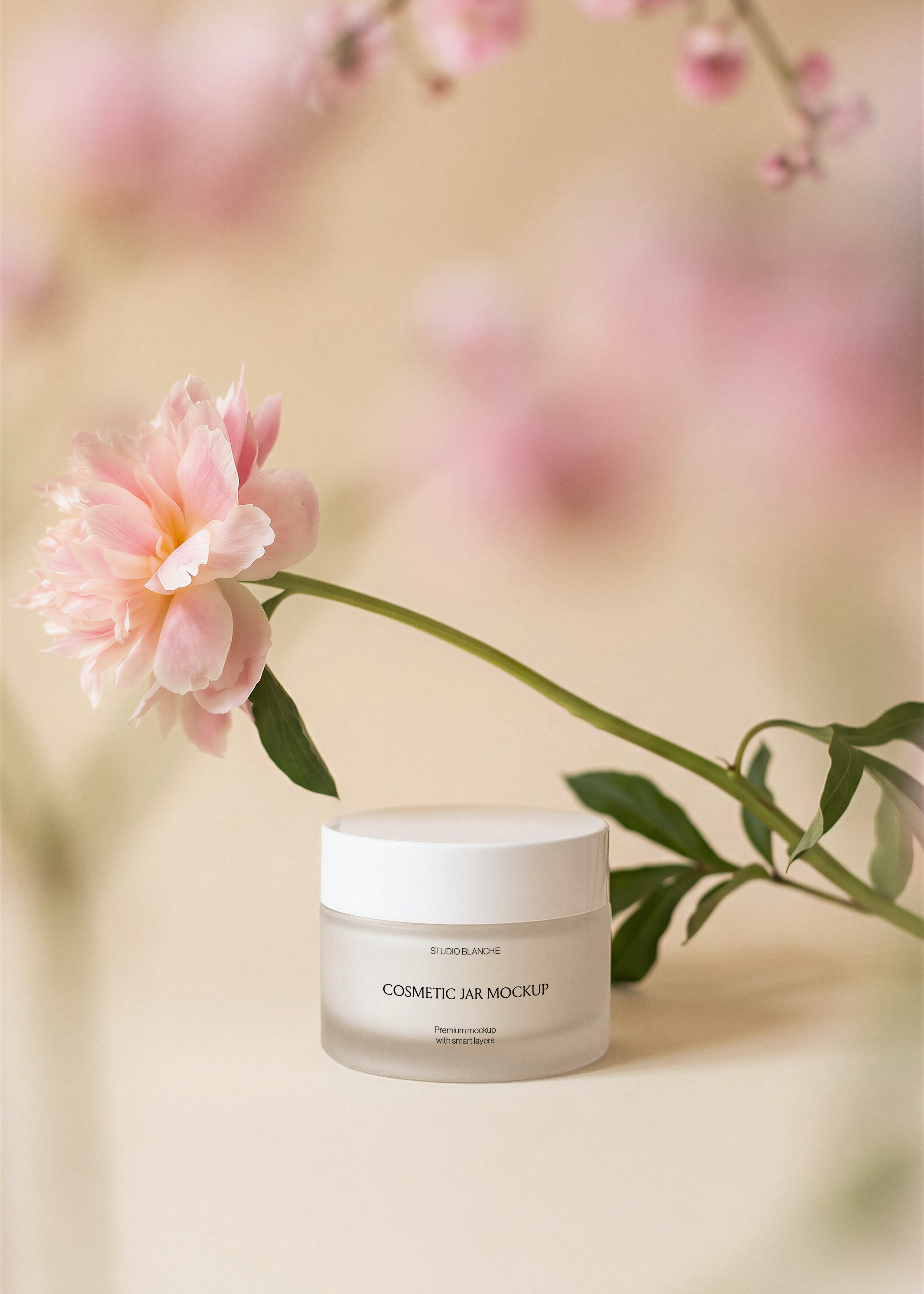 Frosted cosmetic jar mockup showing label area, arcing pink peony stem, soft pink blossom background, beige surface and warm light