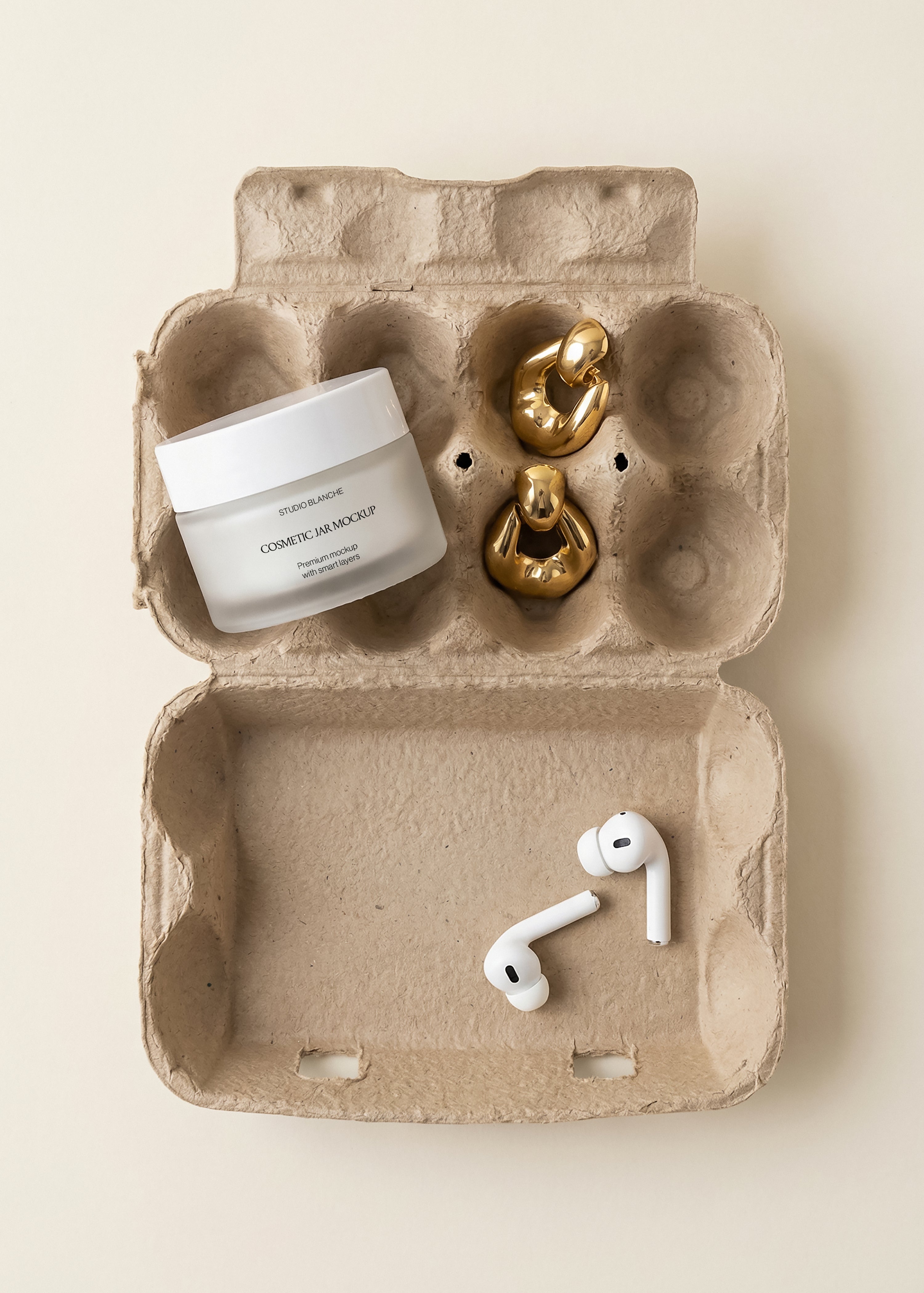 Overhead egg carton flat-lay with frosted cosmetic jar mockup, chunky gold earrings and white earbuds