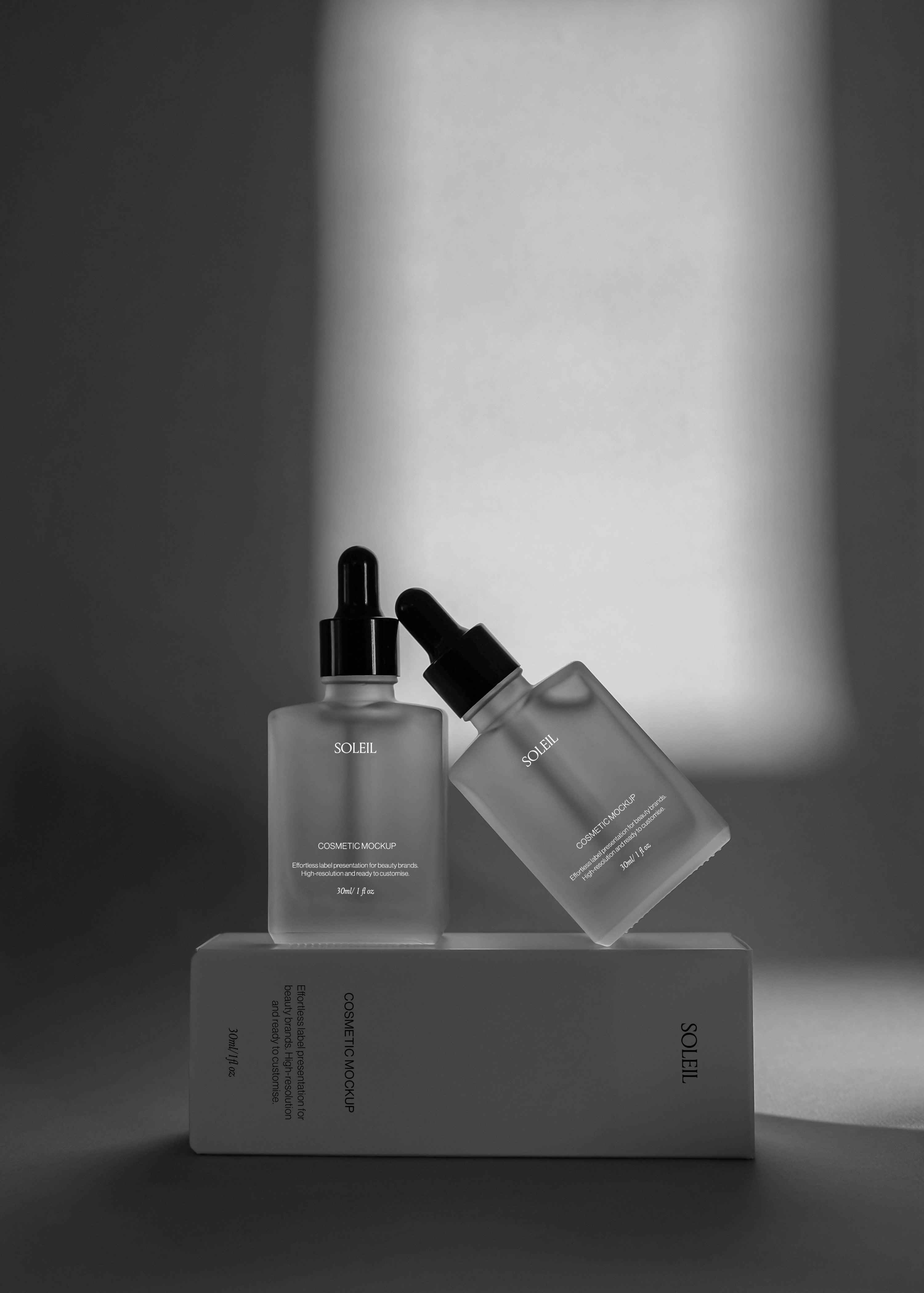 Two amber dropper bottles balanced on a cosmetic box, one upright and one leaning, warm backlit glow against dark backdrop
