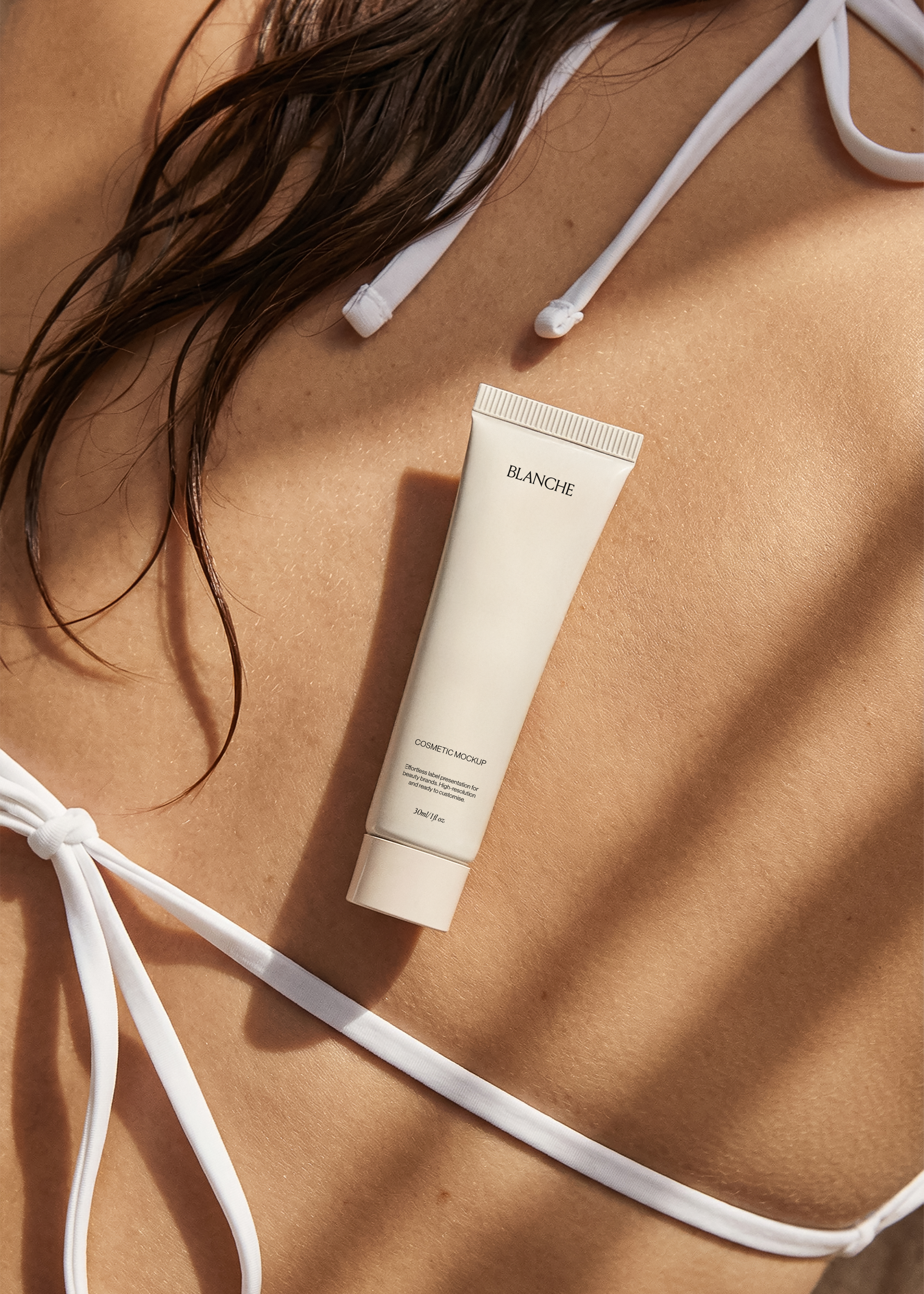 Cream cosmetic tube mockup resting on a sun-warmed back beside white bikini ties, warm editorial styling