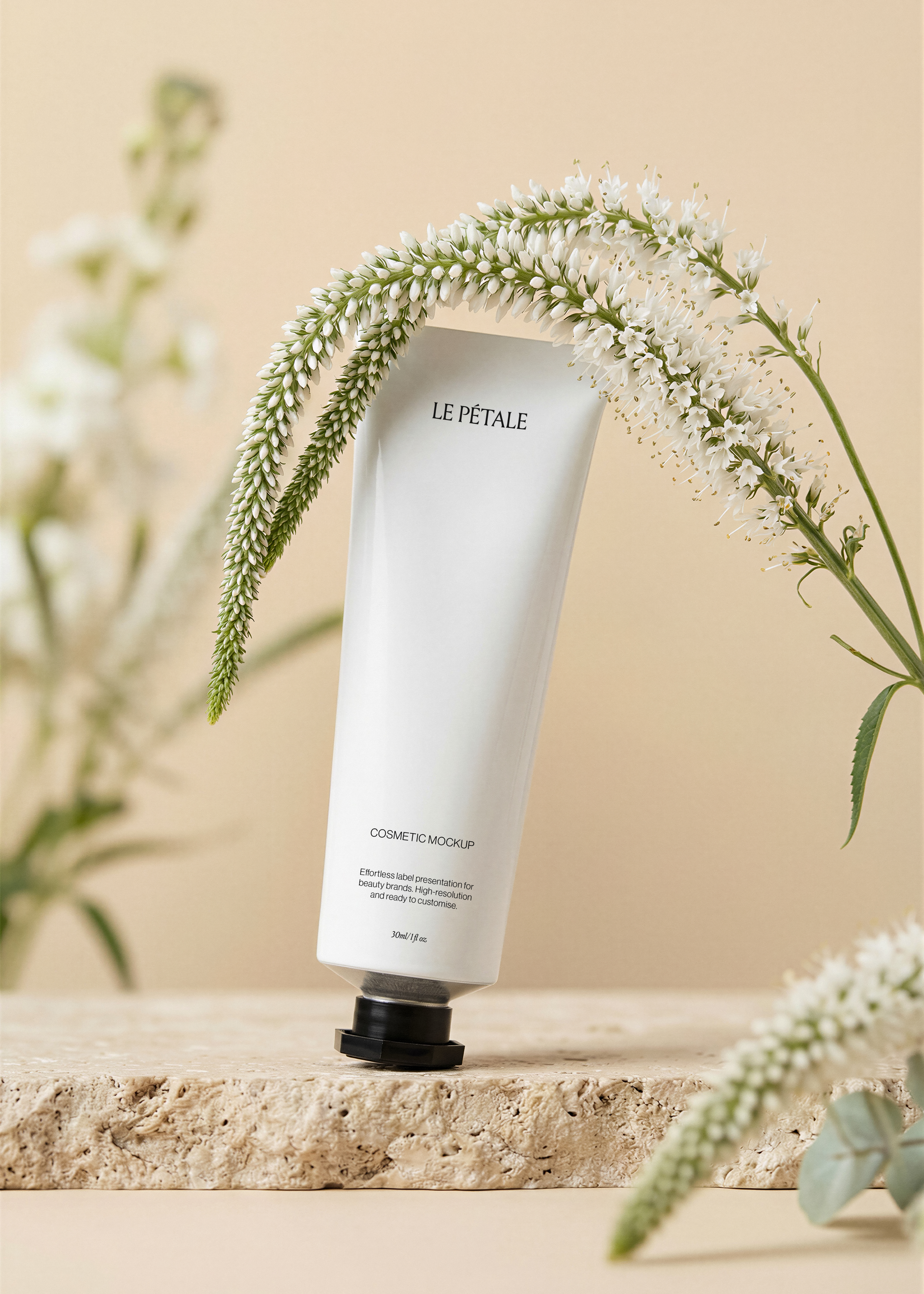 Cosmetic tube mockup with label, raw travertine plinth, white veronicastrum fronds overhead, wildflower stems, sand backdrop