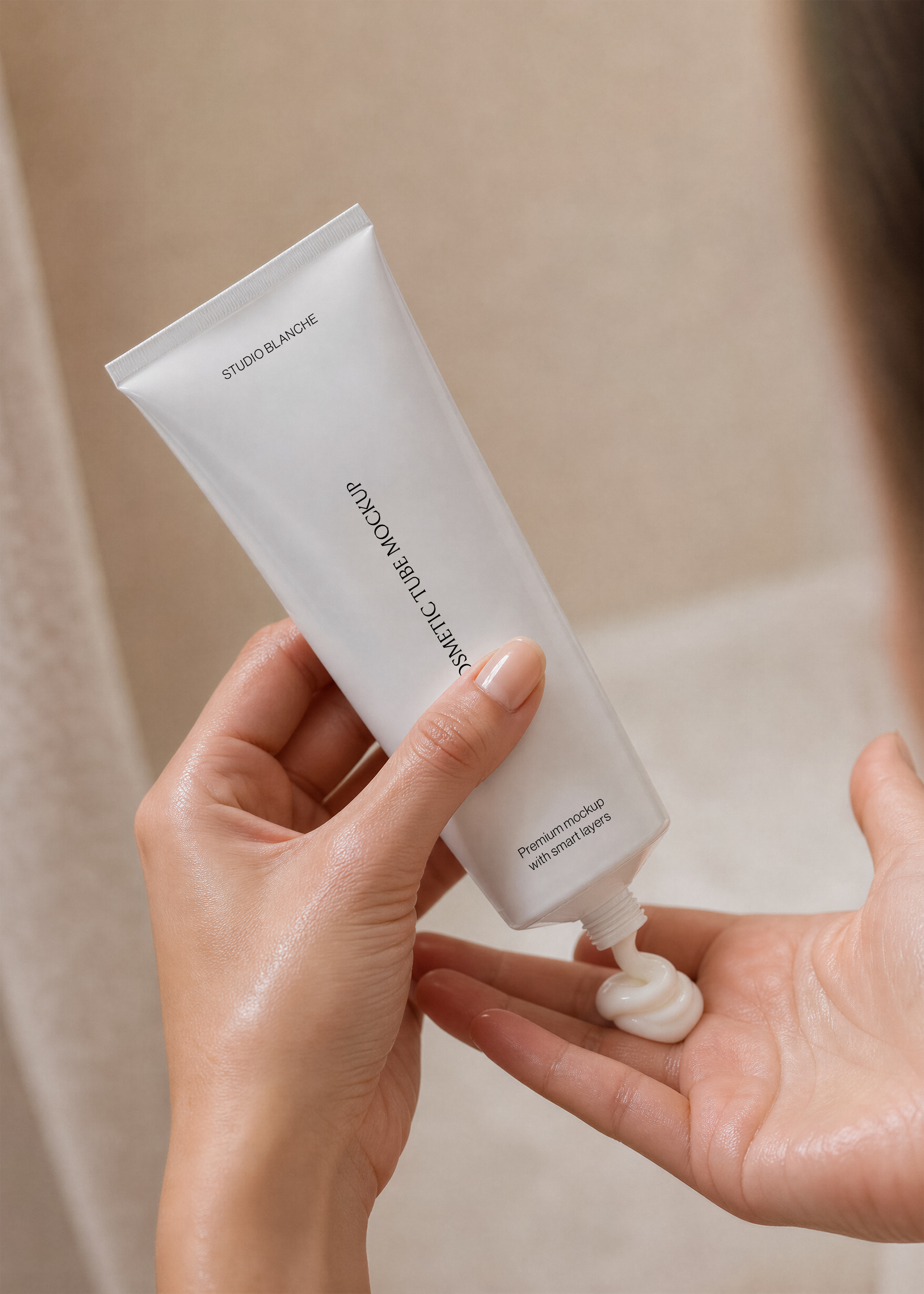 Close view of white cosmetic tube mockup with minimal black label held in two hands, cream swirl in palm, warm lighting