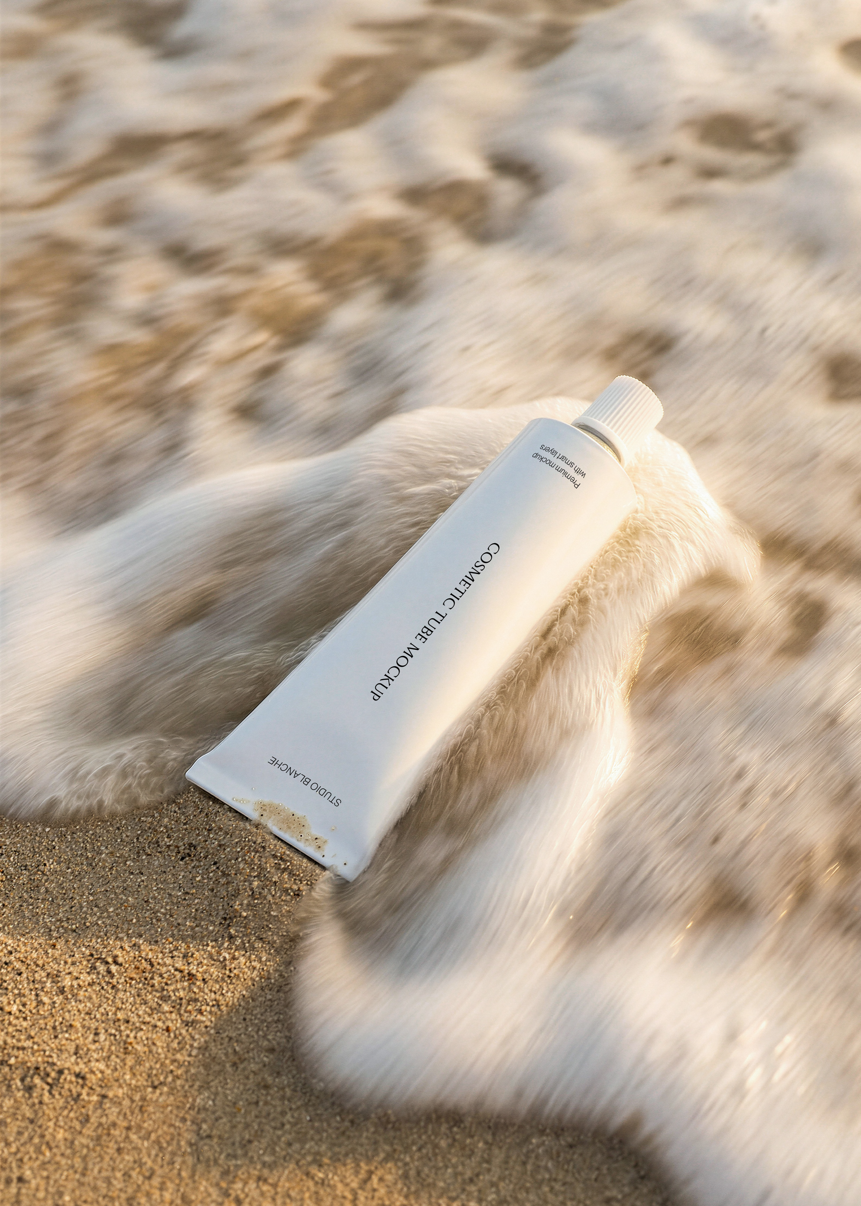 White cosmetic tube mockup resting diagonally in sand with a foaming wave moving across it at golden hour