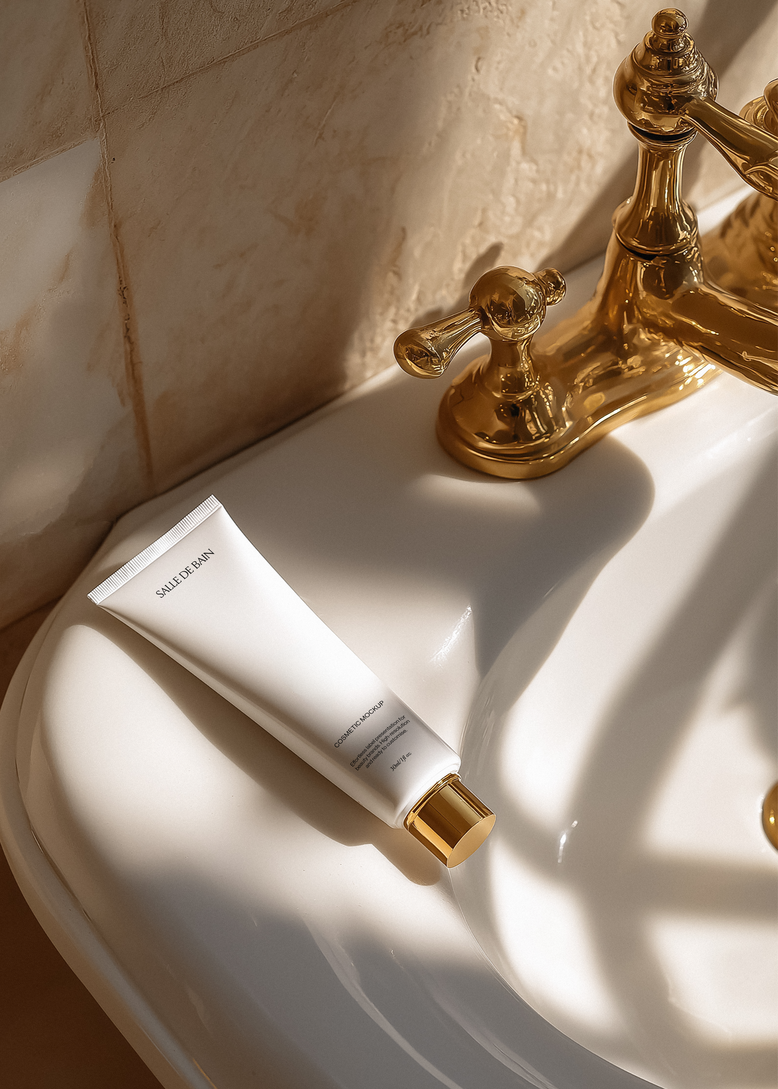White cosmetic tube mockup with gold cap resting on porcelain sink beside antique brass tap, warm editorial bathroom light
