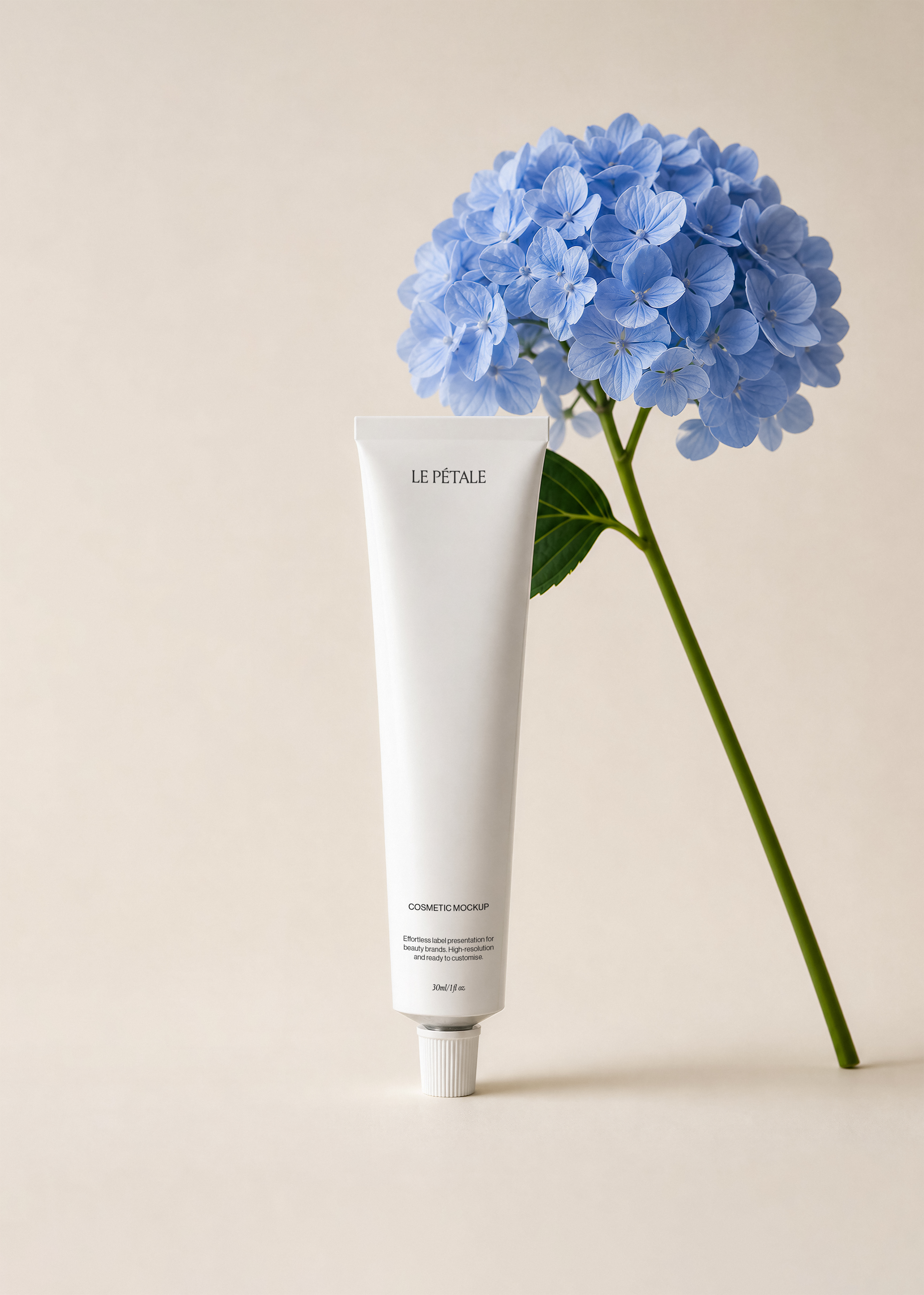 Cosmetic tube mockup with branded label standing beside blue hydrangea stem on warm neutral background, minimal styling