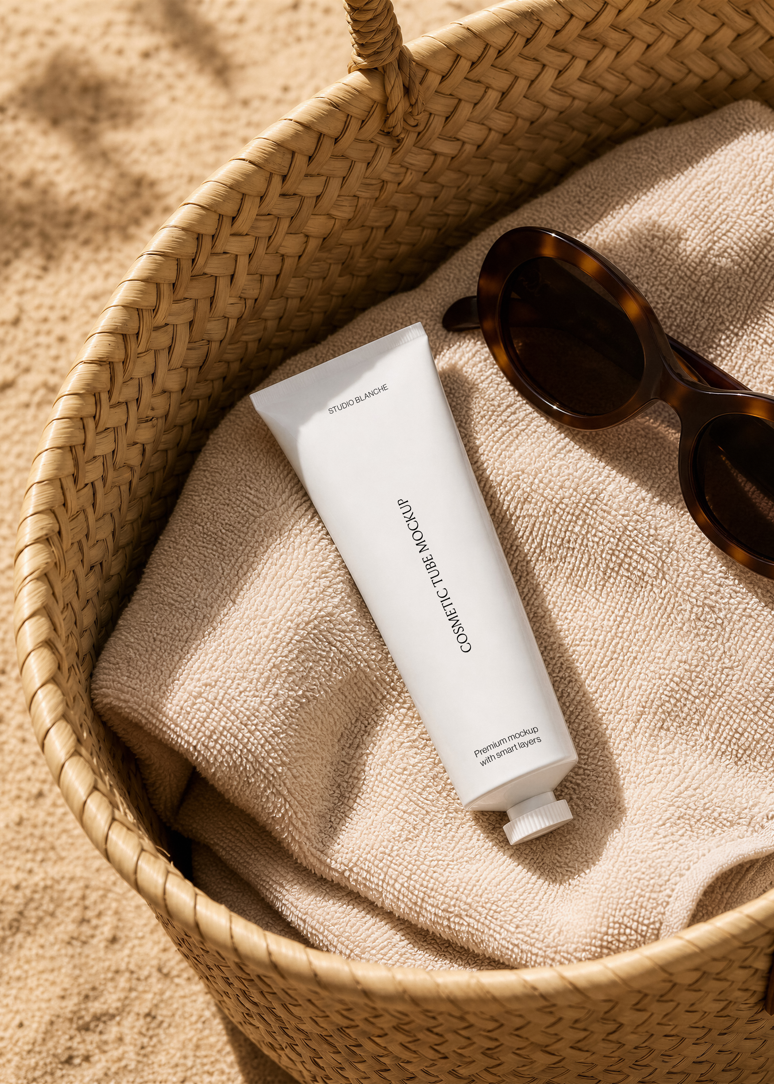 Close view of a white cosmetic tube label on a towel in a straw beach bag, warm sunlit sand, coastal styling