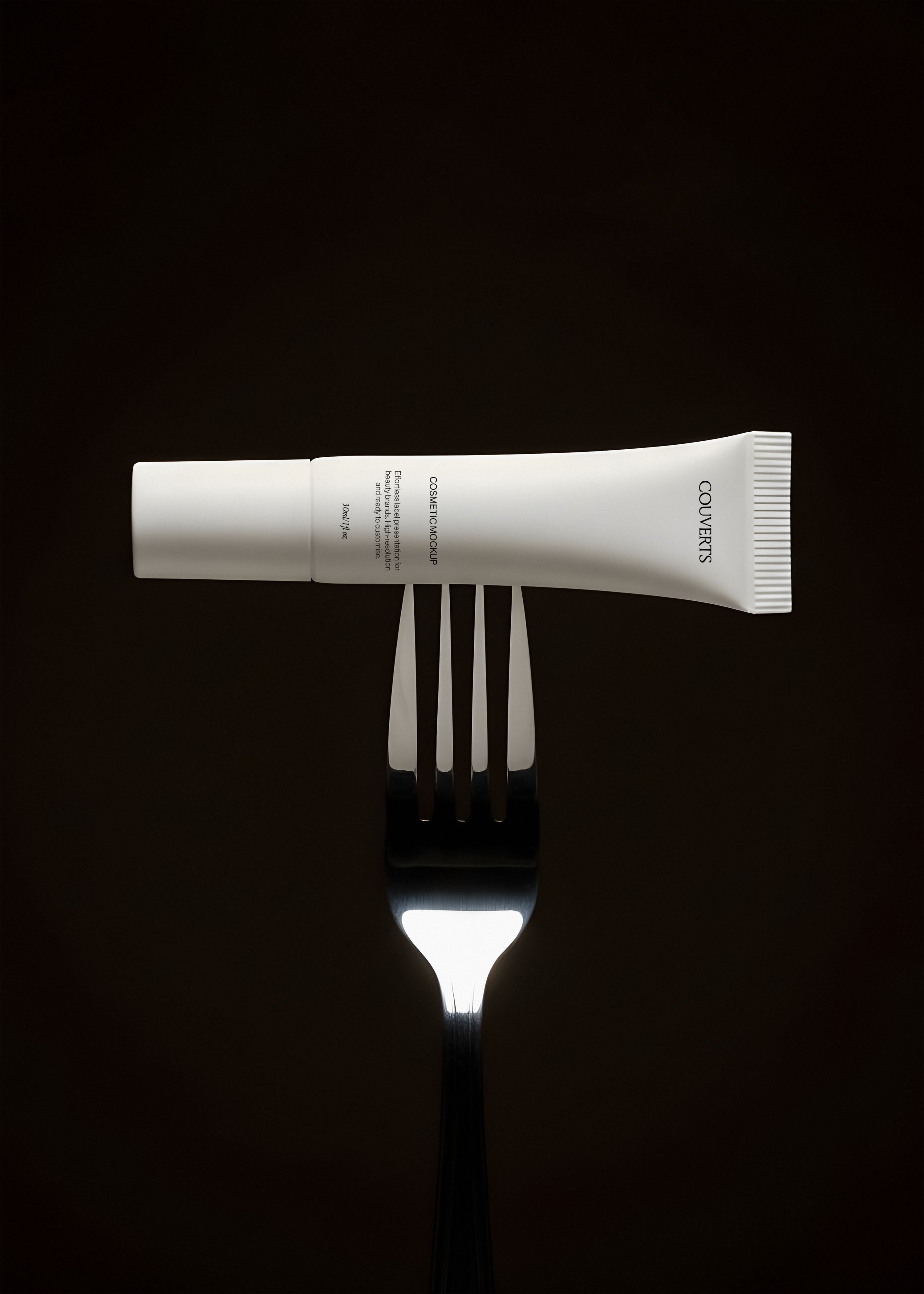 Cosmetic tube mockup balanced across the prongs of a silver fork against a dark brown background, low key lighting