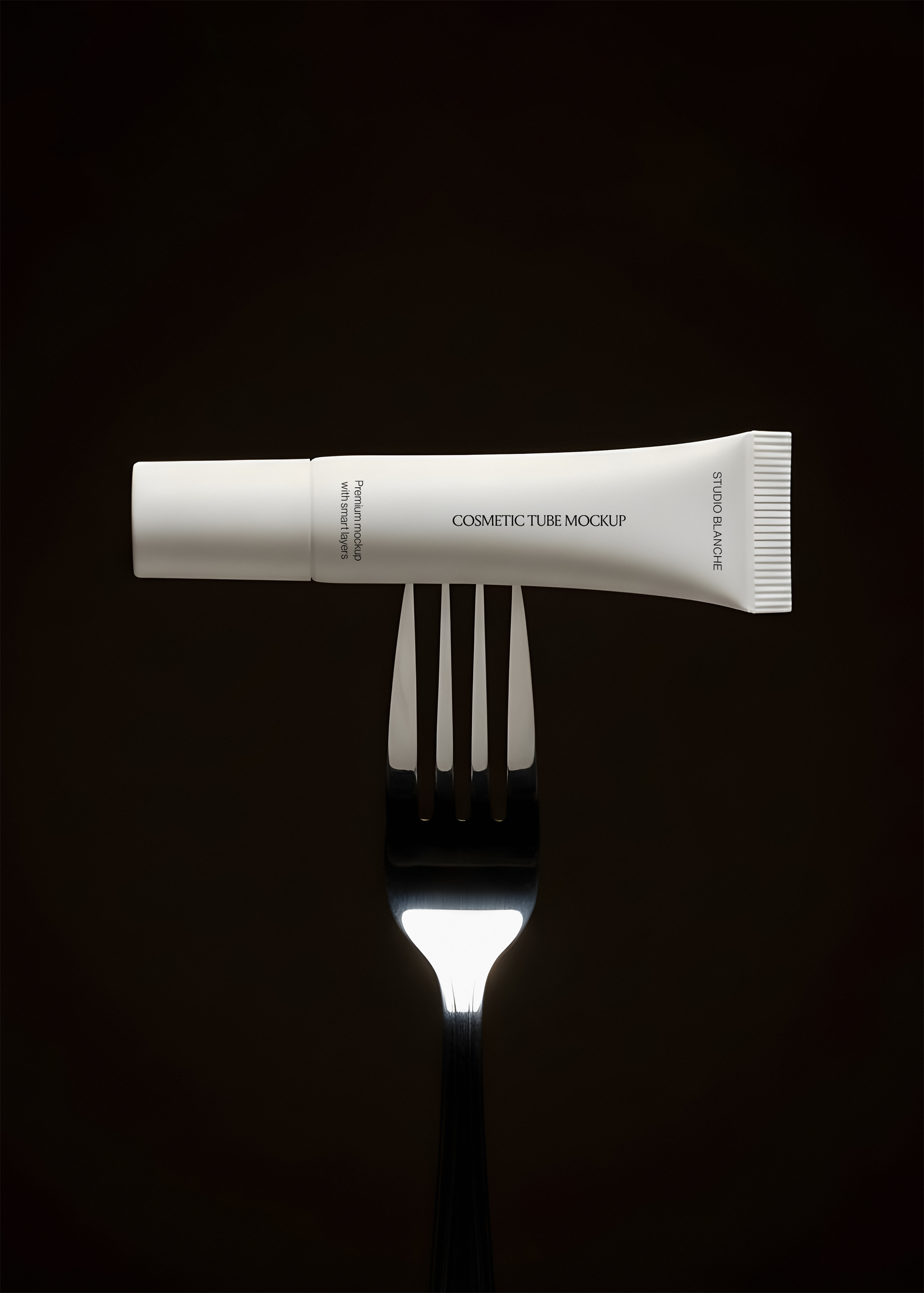 White cosmetic tube mockup resting horizontally on an upright silver fork, dark editorial styling, close view